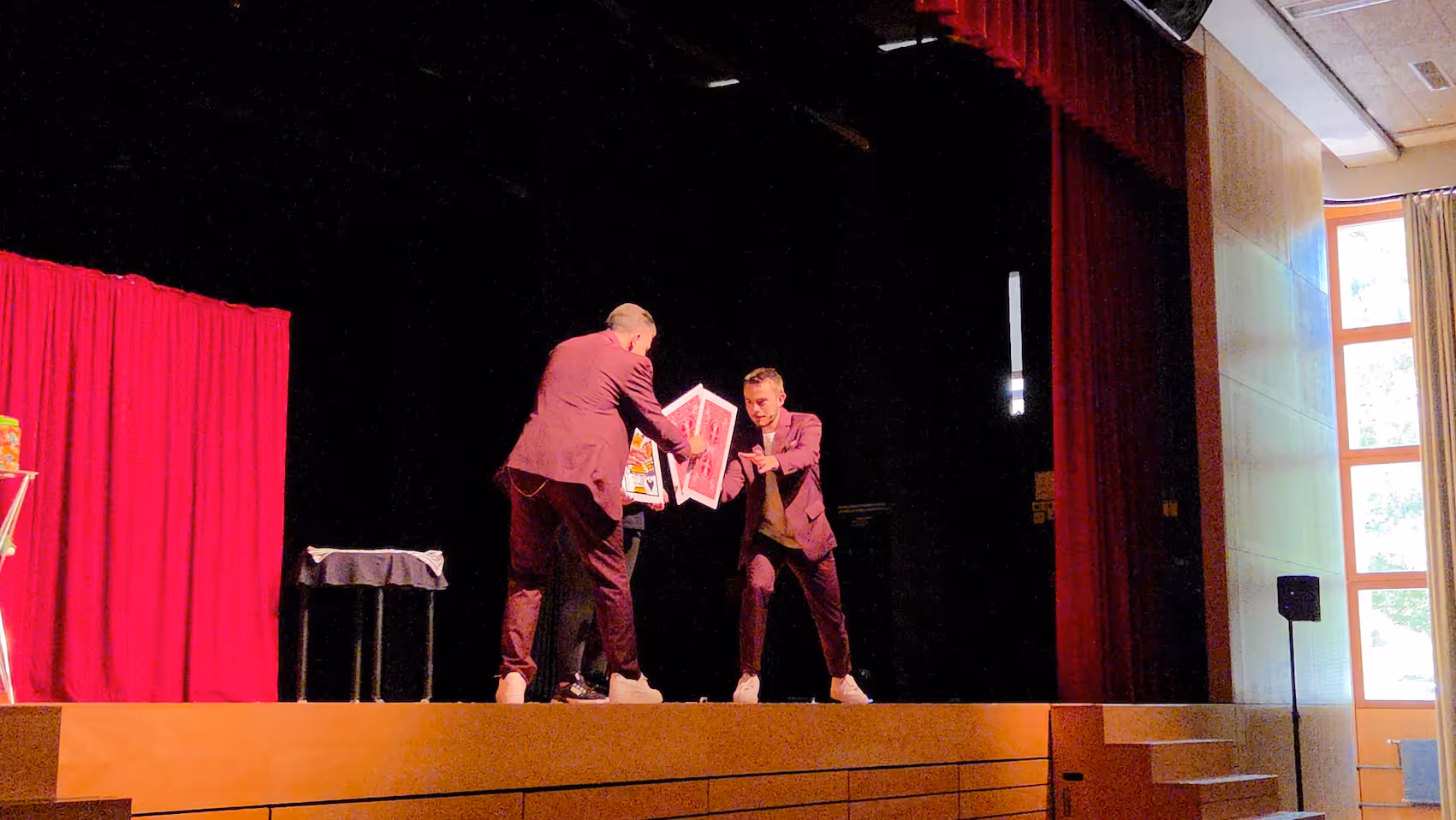 Un duo de magicien présente un tour de carte géante sur une scène.