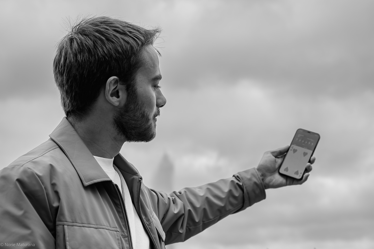 Jeune homme portant une veste montrant une carte sur son téléphone sous un ciel nuageux.