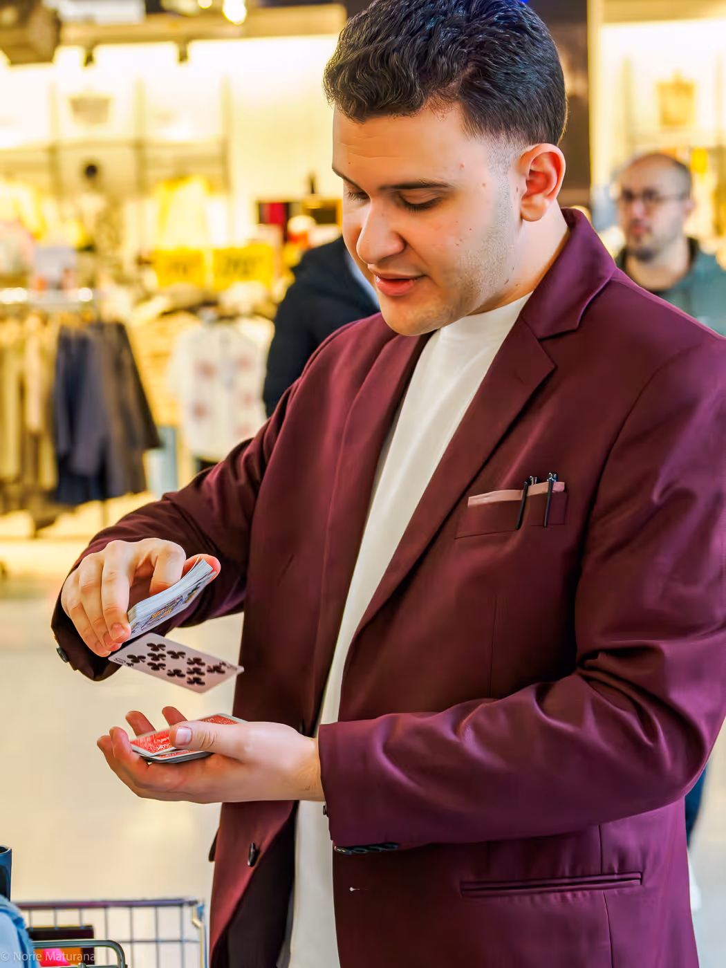Paolo le magicien pratiquant un tour de magie dans un centre commercial a signy centre. il fait une cascade avec un jeux de carte et porte un costume rouge. 