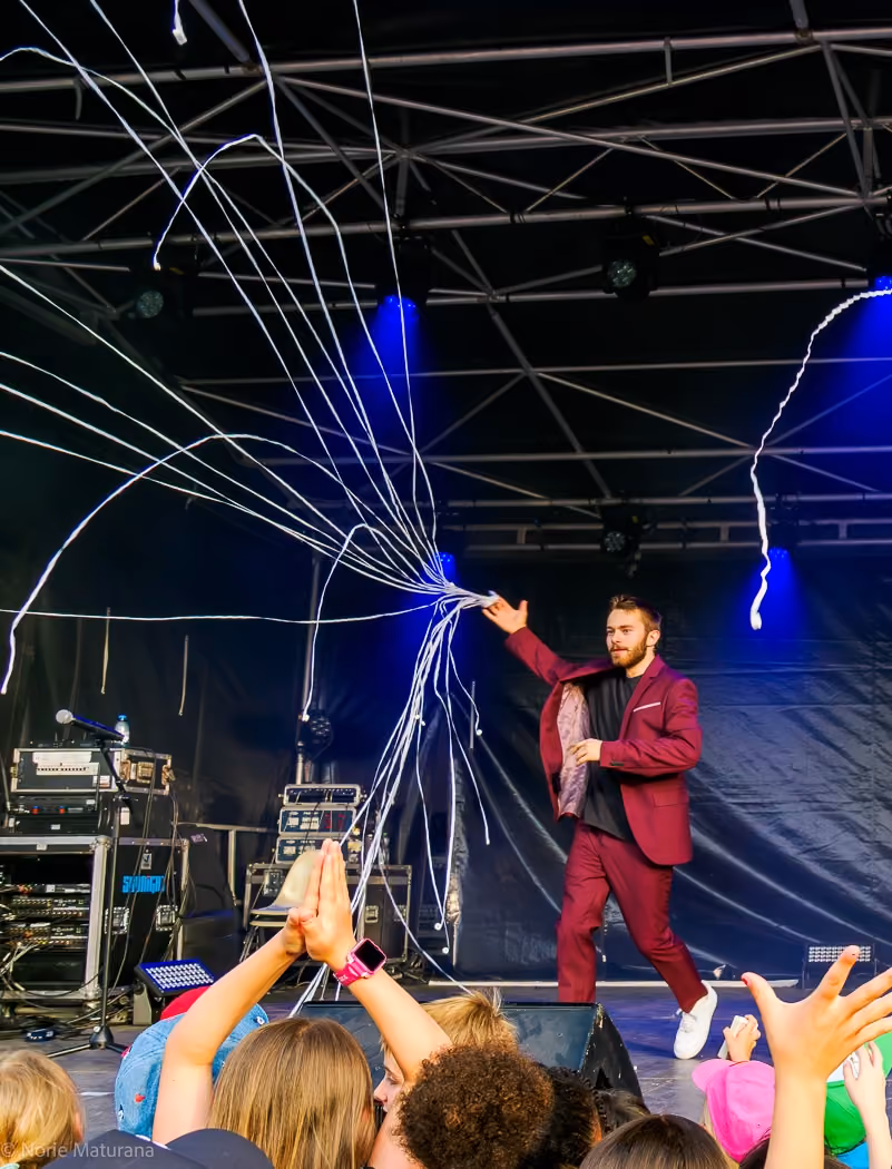Un homme en costume bordeaux sur scène interagit avec un public enthousiaste lors d'un spectacle.
