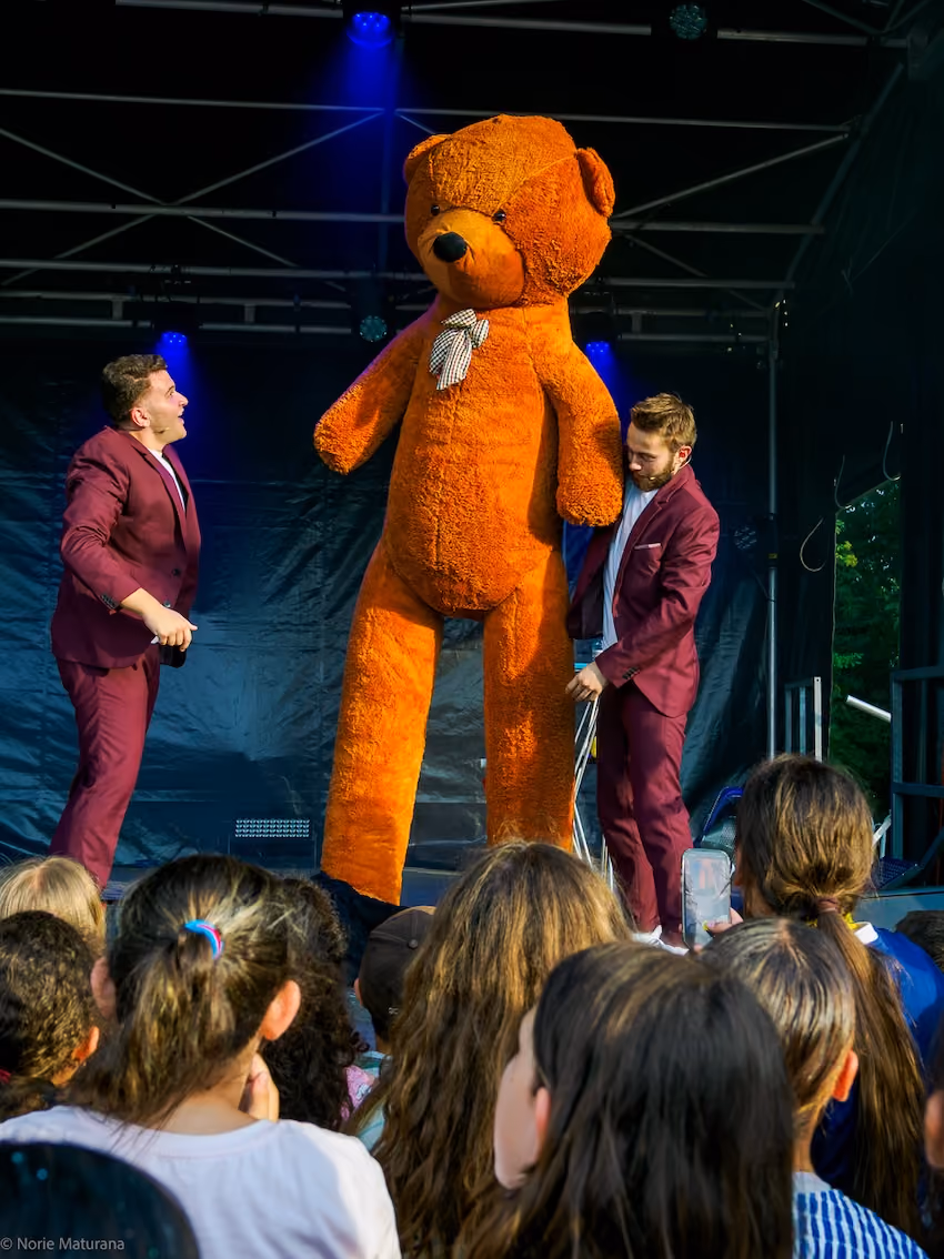 Le duo NP Magiciens fait apparaitre un ours en peluche sur scène devant une foule de personnes.