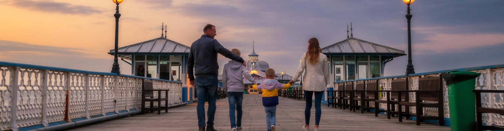 Family walking hand in hand along Llandudno Pier at sunset during February half term holiday.