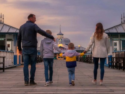 Family walking hand in hand along Llandudno Pier at sunset during February half term holiday.
