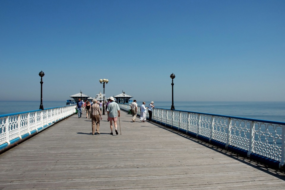 Visitors strolling along Llandudno Pier on a sunny day, with calm blue sea and Victorian pavilion