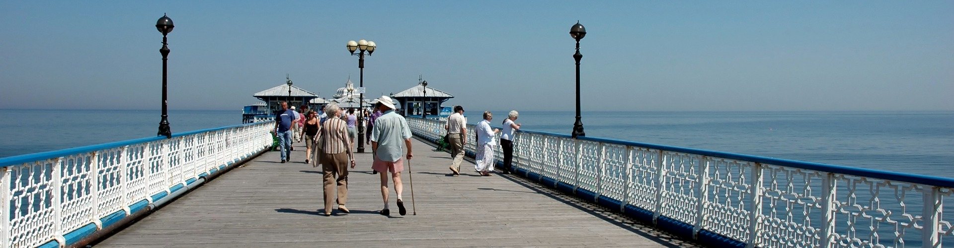 Panoramic view of Llandudno Pier with visitors walking toward the Victorian pavilion and calm sea