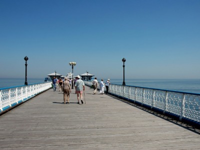 Visitors strolling along Llandudno Pier on a sunny day, with calm blue sea and Victorian pavilion