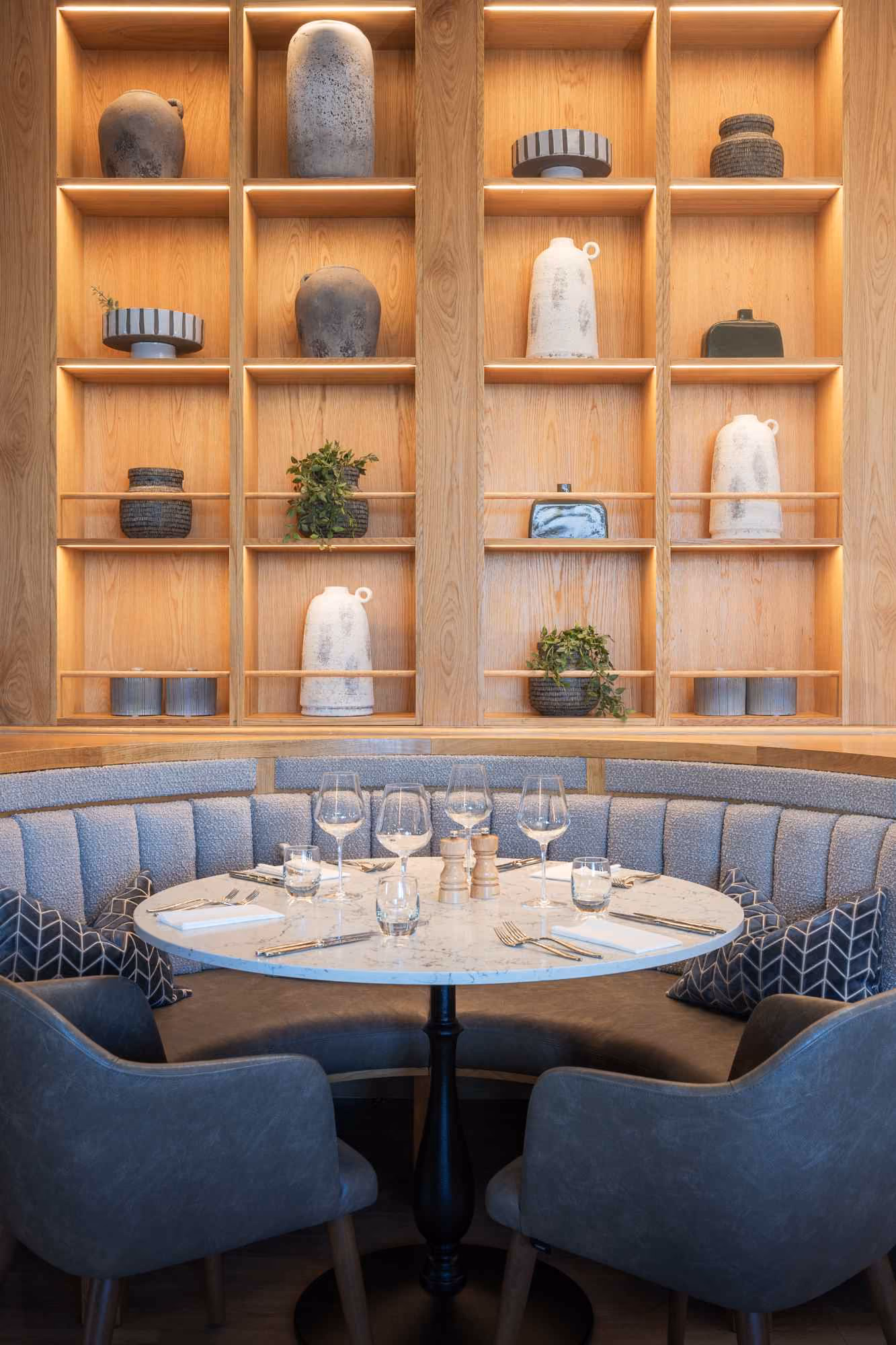 Round dining table with blue banquette seating beneath display shelves at The Goat restaurant, Llandudno