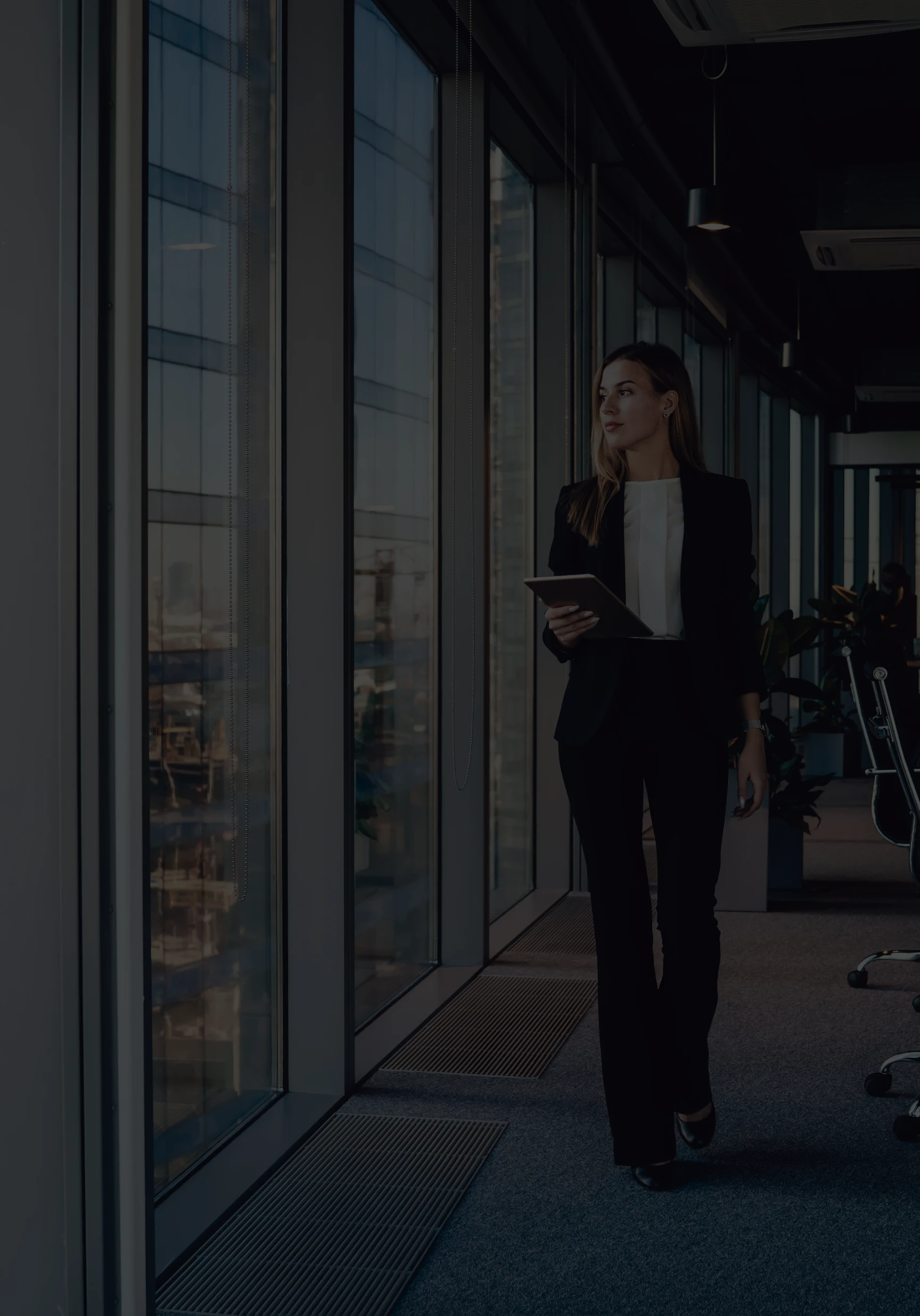 Premium executive services and corporate leadership: A female professional in a business suit walking past floor-to-ceiling windows in a modern office, illustrating high-stakes logistics and executive-level performance.