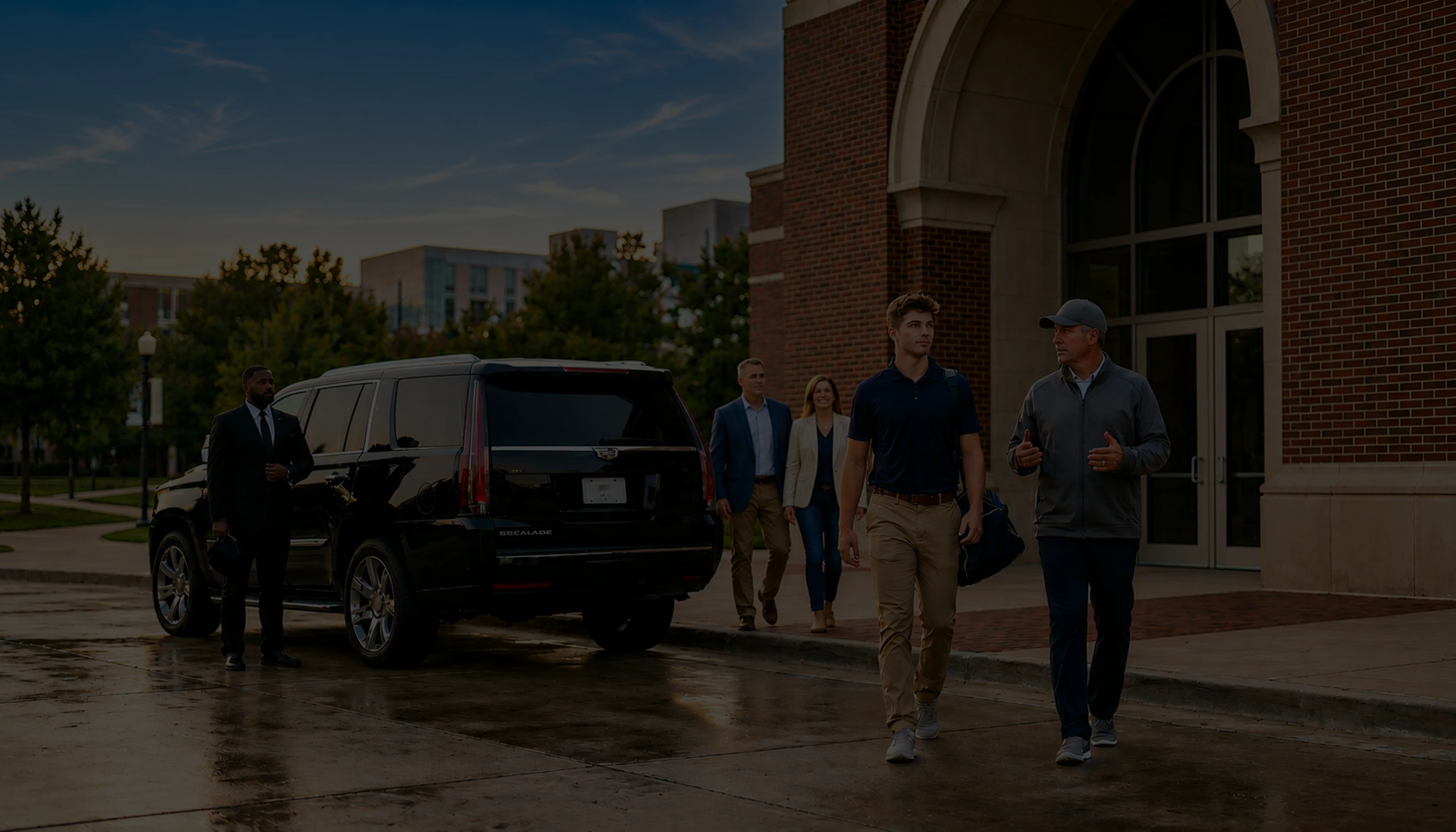 Savoya premium SUV service: A professional chauffeur waits with a luxury black SUV for clients arriving at a corporate office or university campus venue.