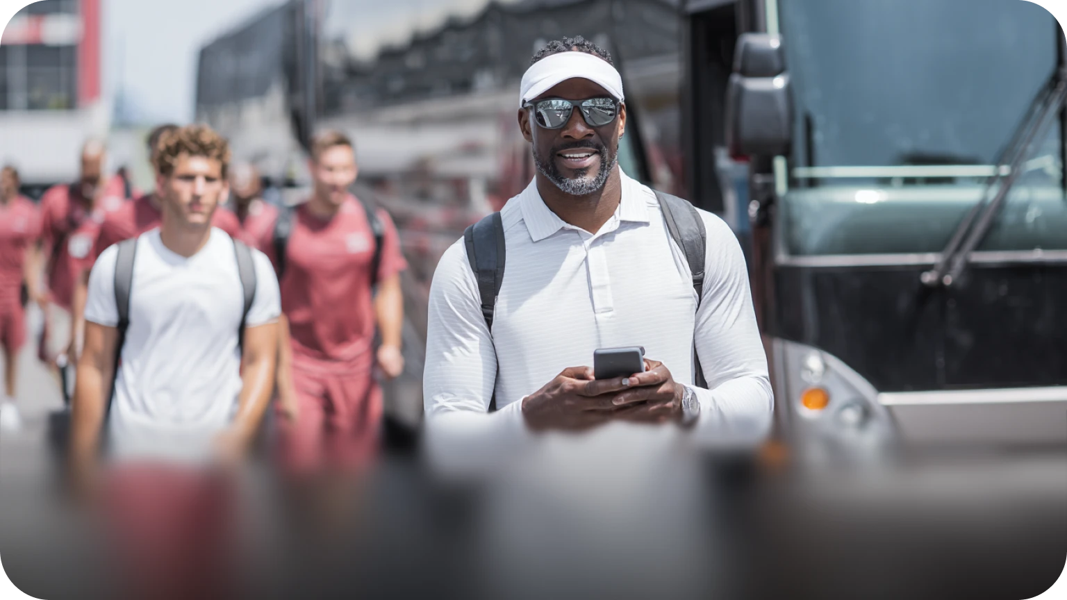 Savoya athletic team travel: A sports professional managing logistics on a mobile device as a team prepares to board a premium chauffeured charter bus.