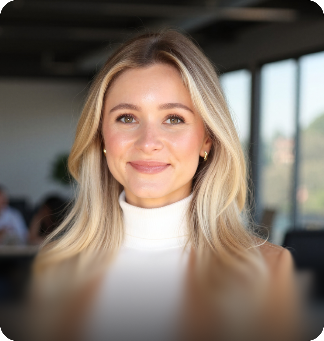 Professional headshot of a smiling woman with long blonde wavy hair, wearing a white turtleneck and a tan blazer.