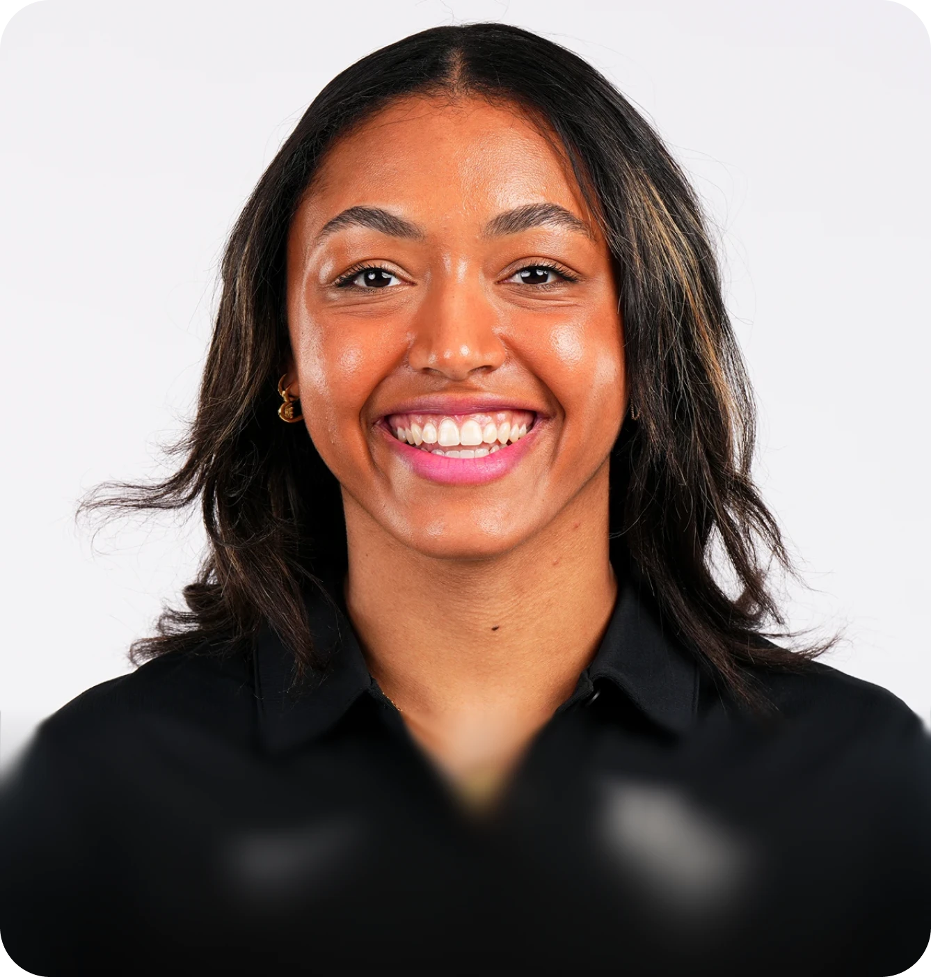 Professional headshot of a smiling woman with dark hair, wearing a black polo shirt against a plain light background.