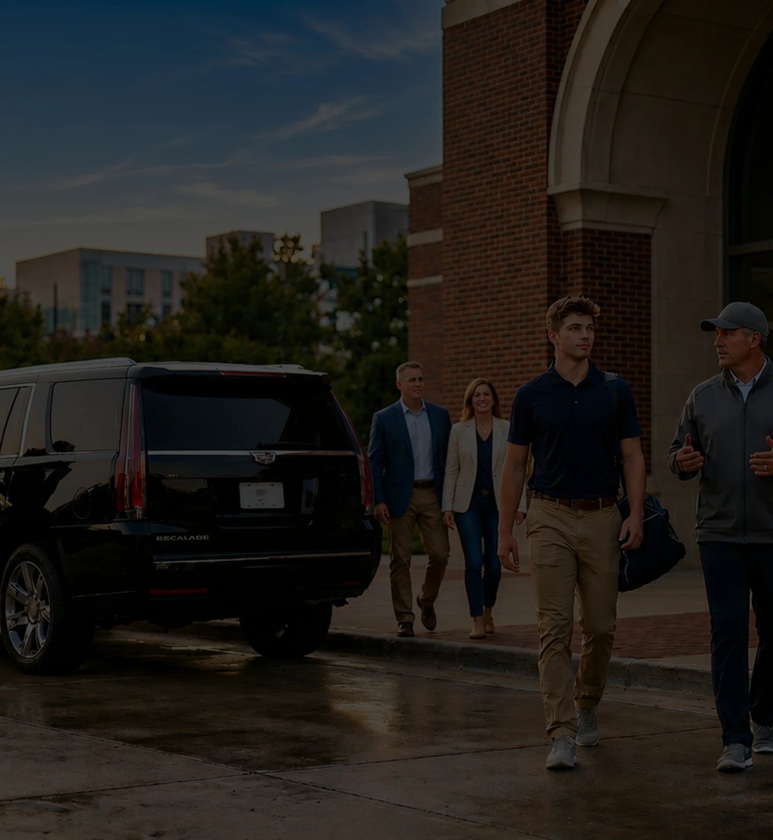 A group of professional travelers walking toward a black luxury SUV parked in front of a brick building entrance.