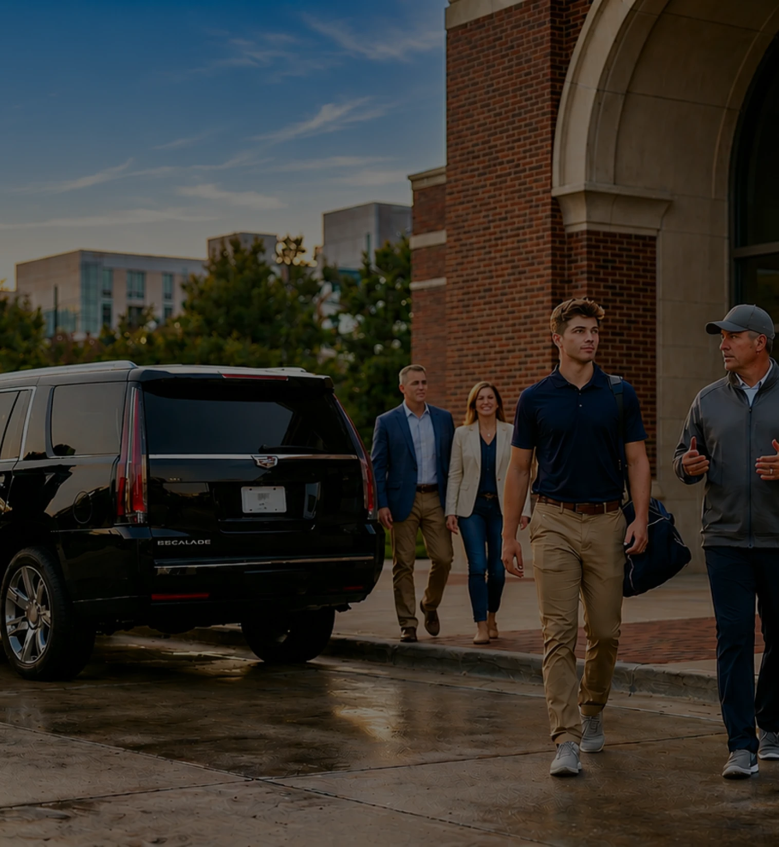 A group of professional travelers walking toward a black luxury SUV parked in front of a brick building entrance.