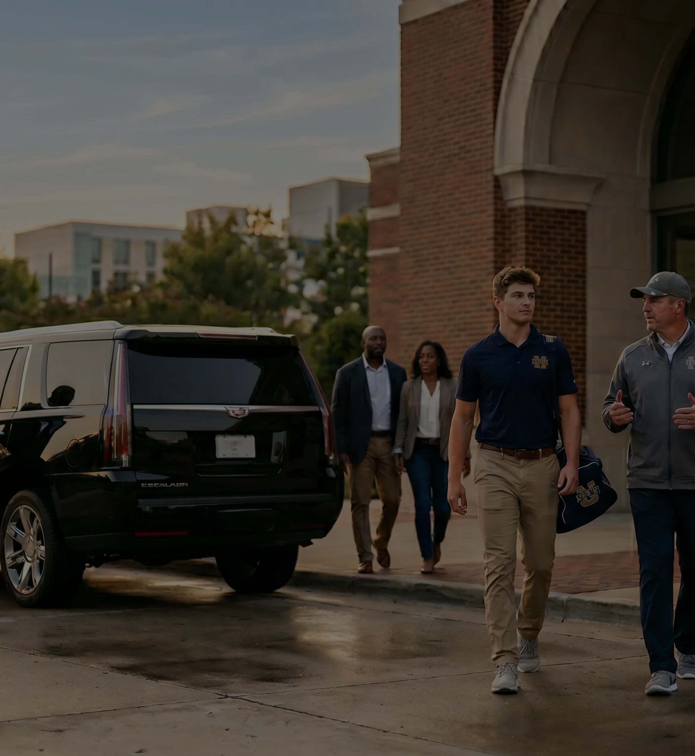 A group of professional travelers walking toward a black luxury SUV parked in front of a brick building entrance.