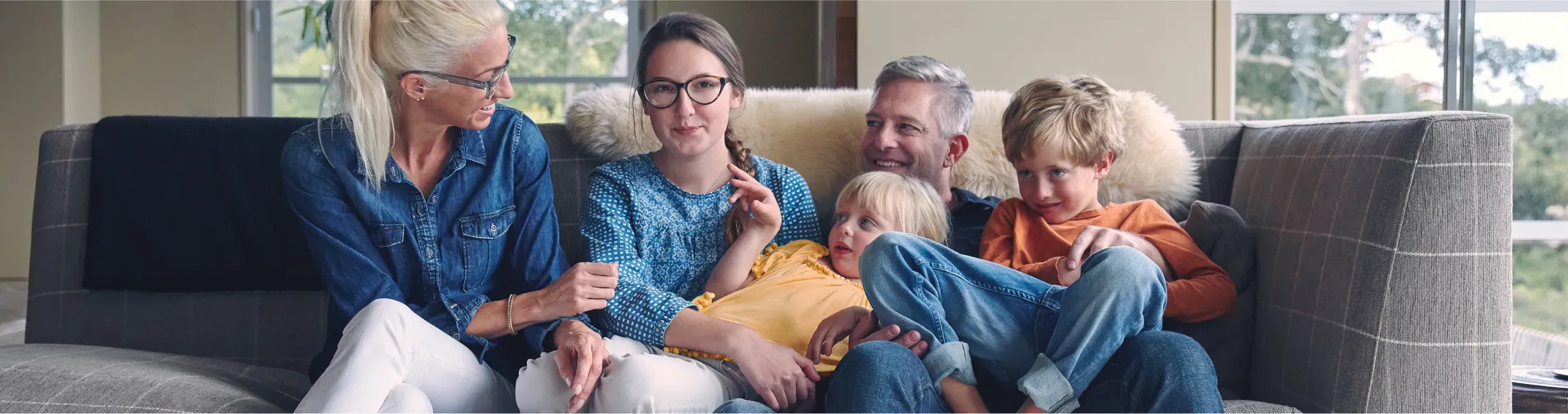 Five people sitting together on a couch, smiling and engaging with each other in a cozy living room.