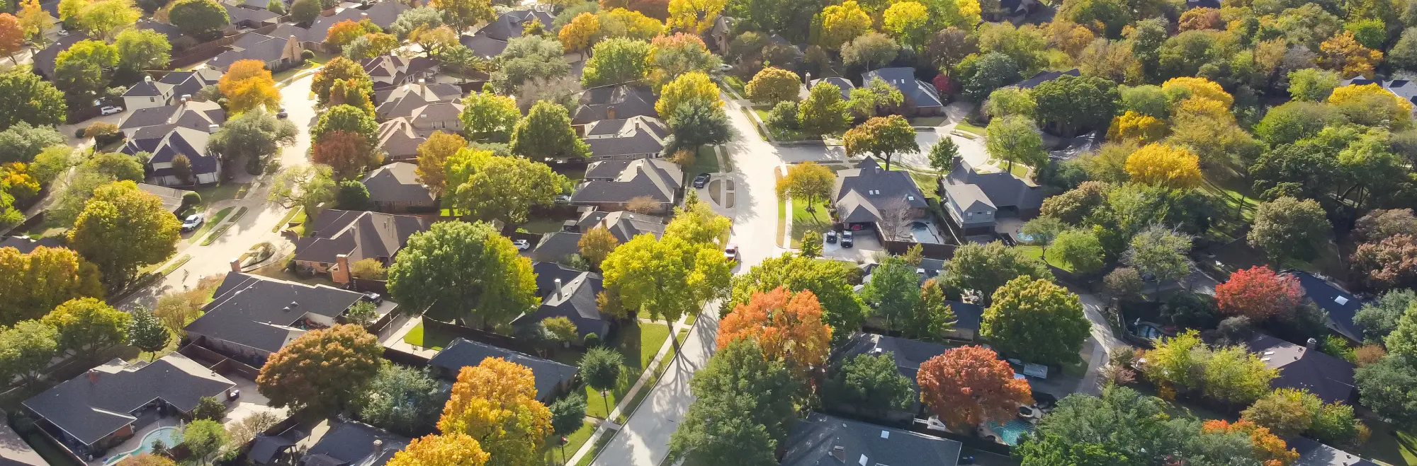 Aerial view of a suburban neighborhood with houses, streets, and trees showing autumn colors.