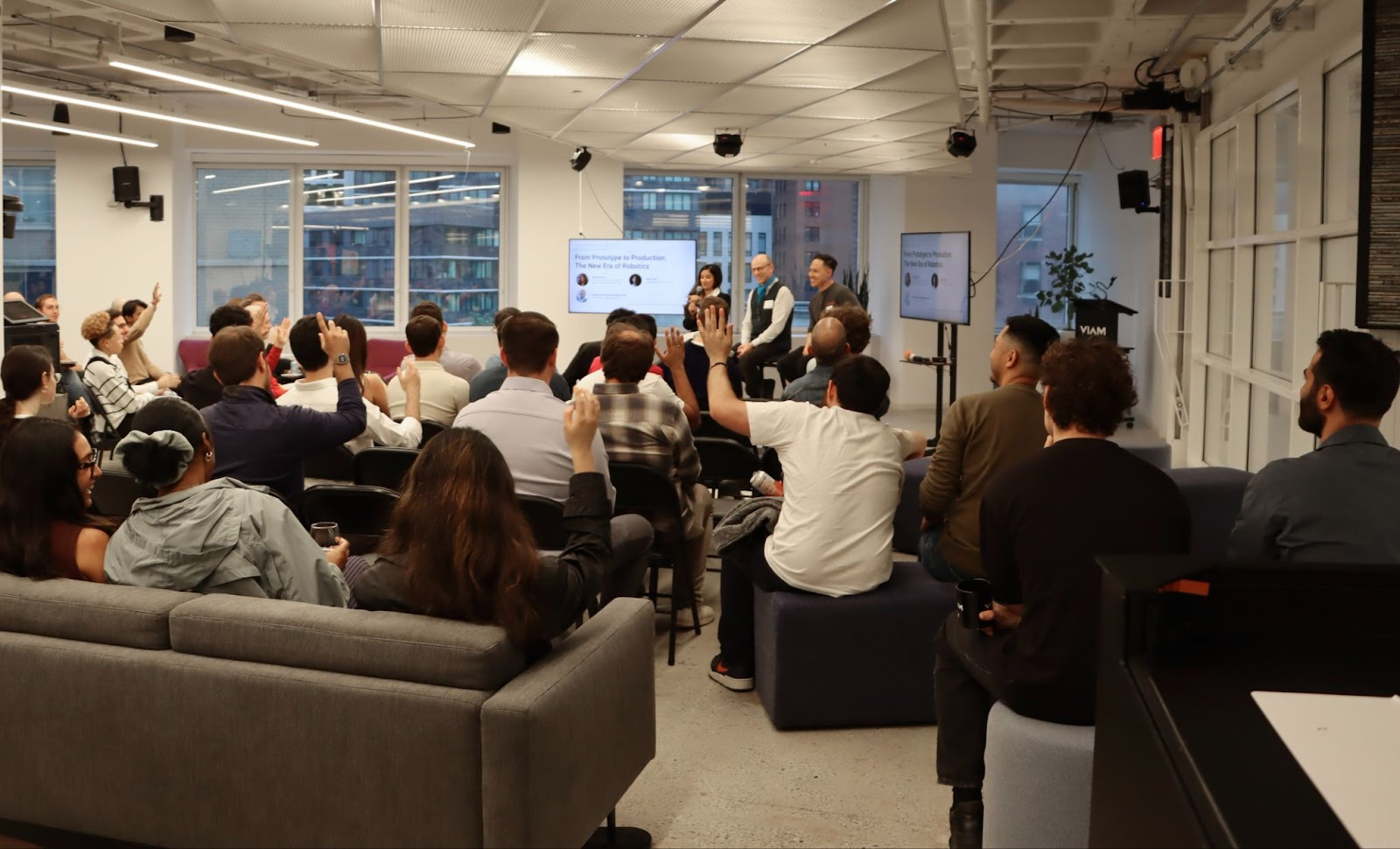 Panel speakers sitting in front of a crowd of attendees raising their hands to ask questions