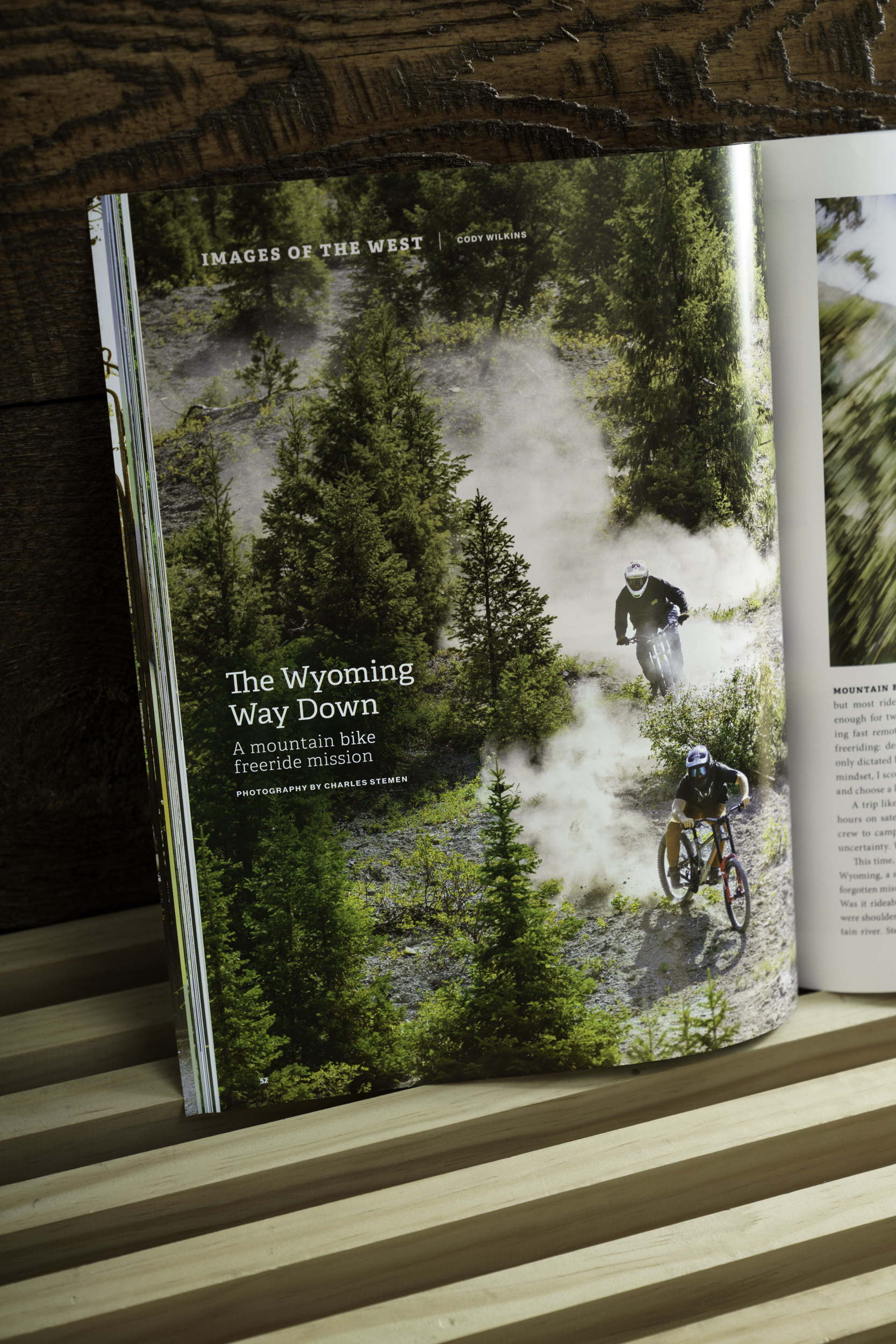 Big Sky Journal feature showing mountain bikers descending a dusty trail through a forest in Wyoming.