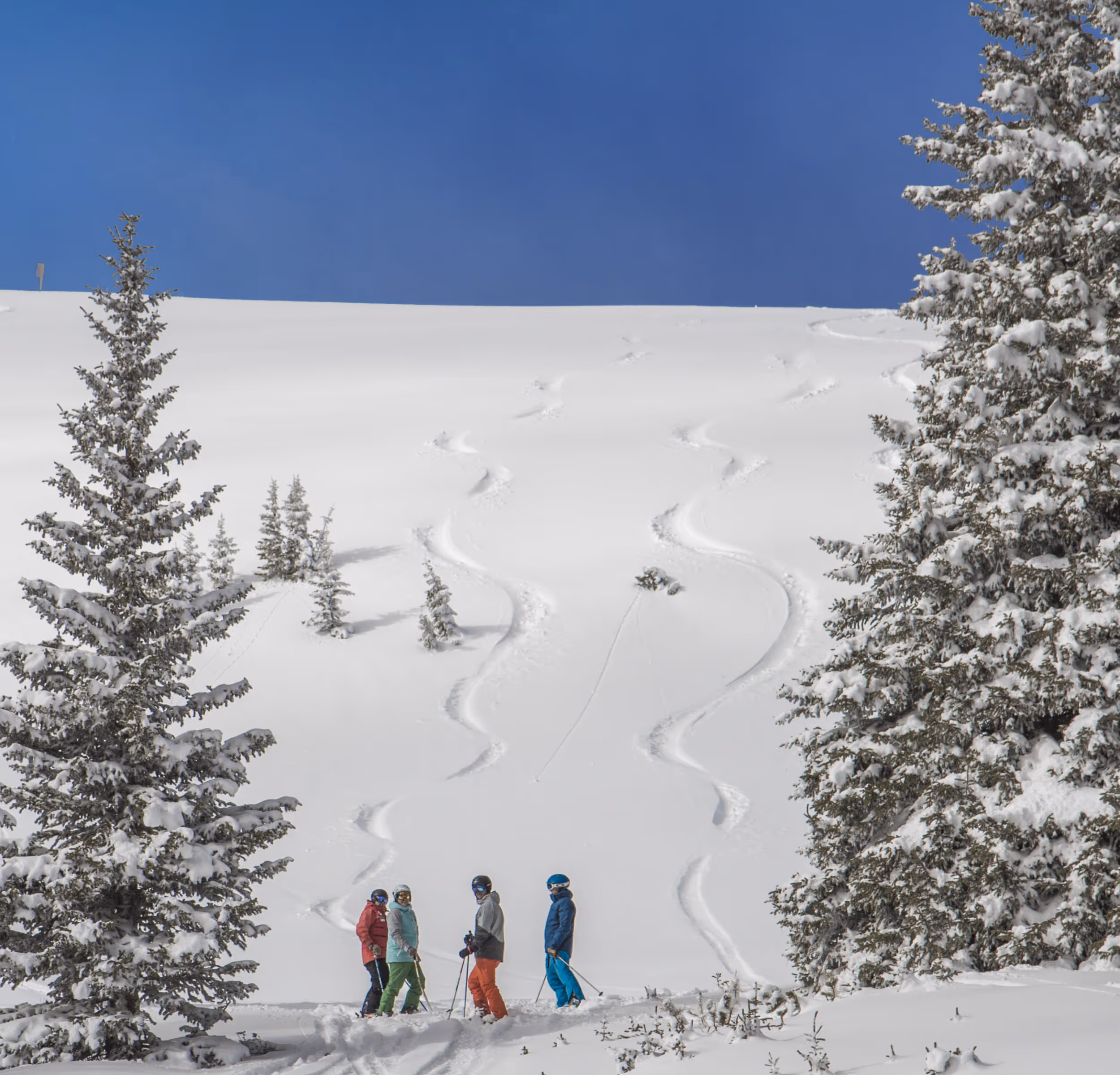 Some skiers admiring their turns in the snow at the bottom of a ski run 