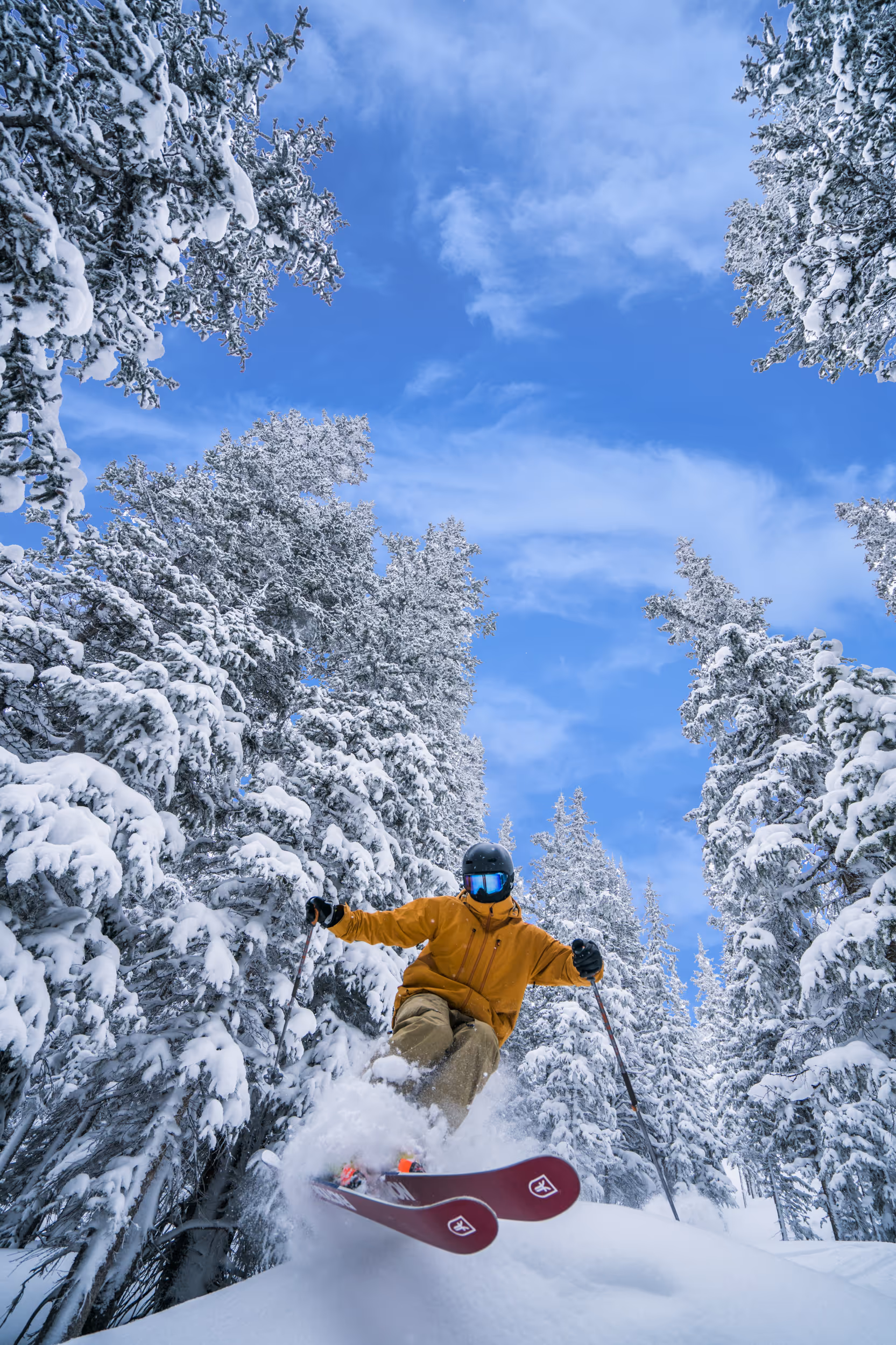 A sick action shot of a skier with a bright yellow jacket and red skis popping through the snow on a POW day 