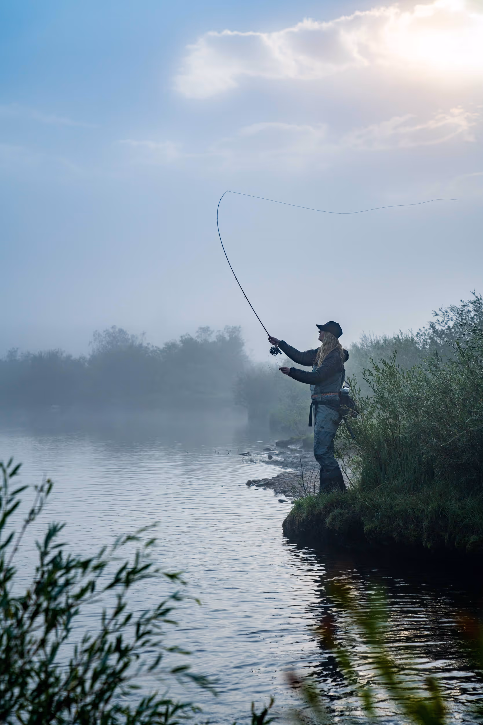 A fly fisher woman casting out her line from the foggy bank