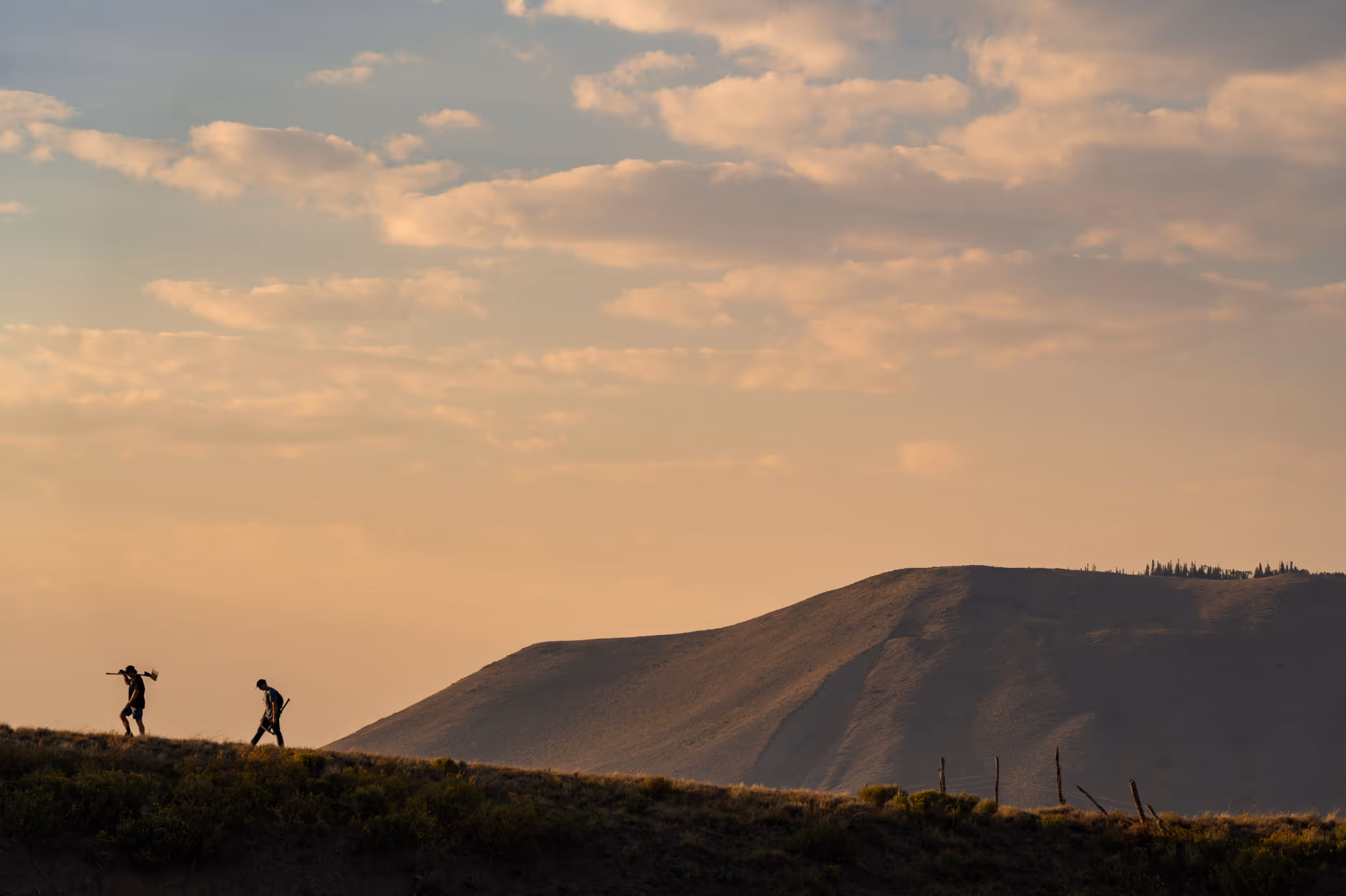 A silhouette of some mountain bikers walking across a ridge line just before sunset  
