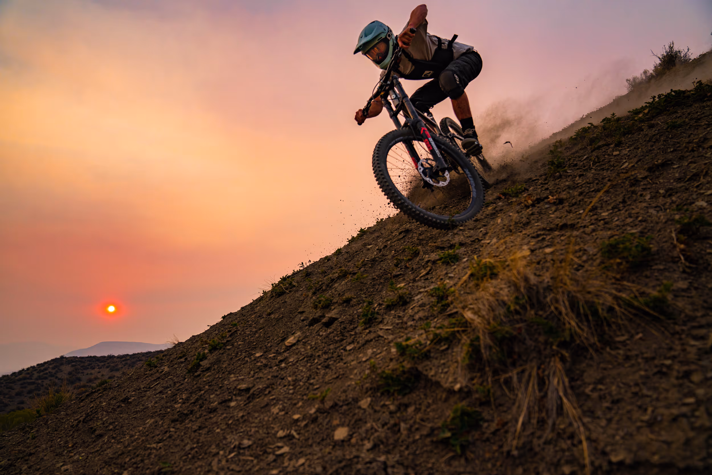A sick sunset shot of a mountain biker coming down a steep dusty trail 