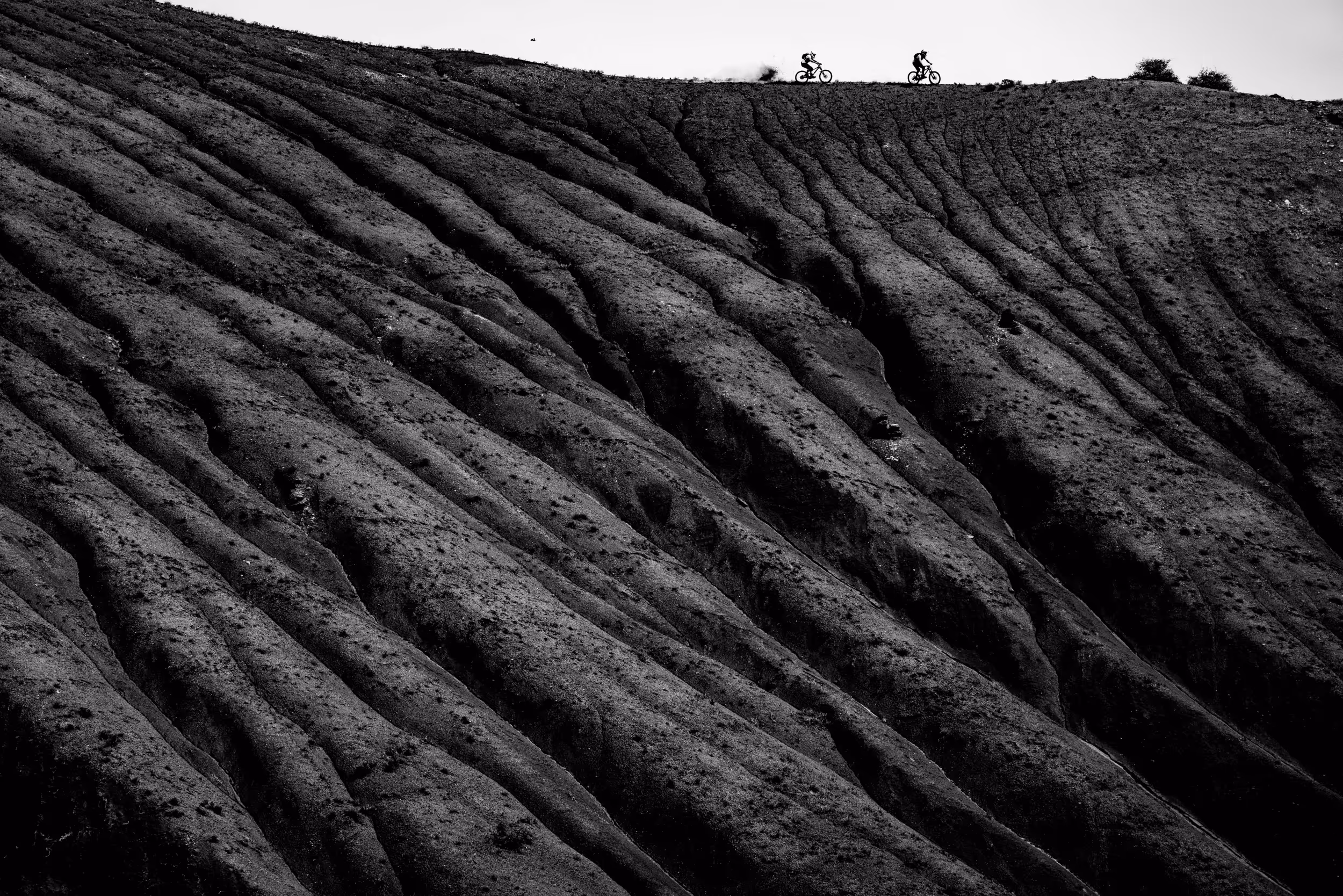 A black and white landscape shot with 2 mountain bikers at the top of a ridge line 