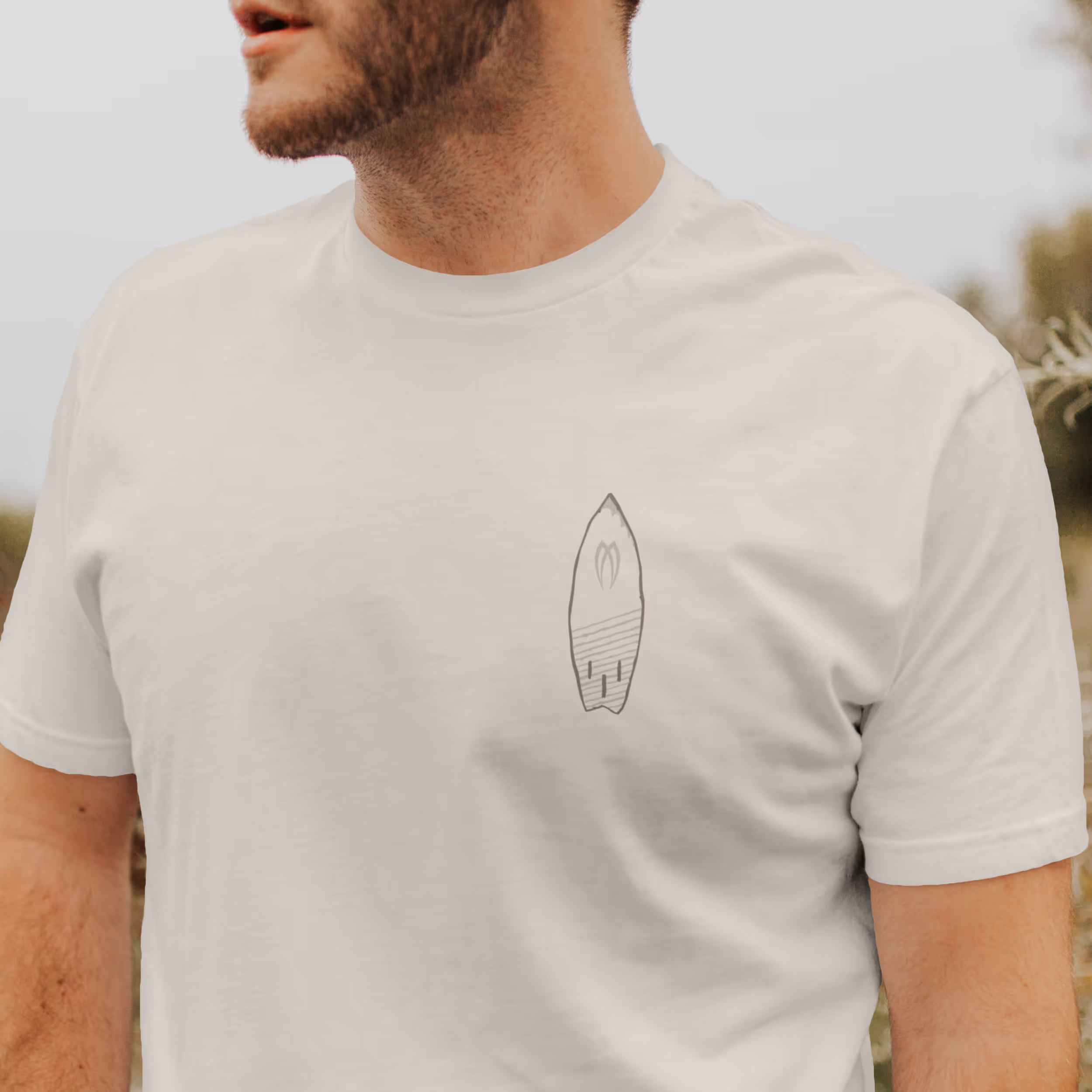 A man wearing a white tshirt with a small surfboard graphic shown on the front 