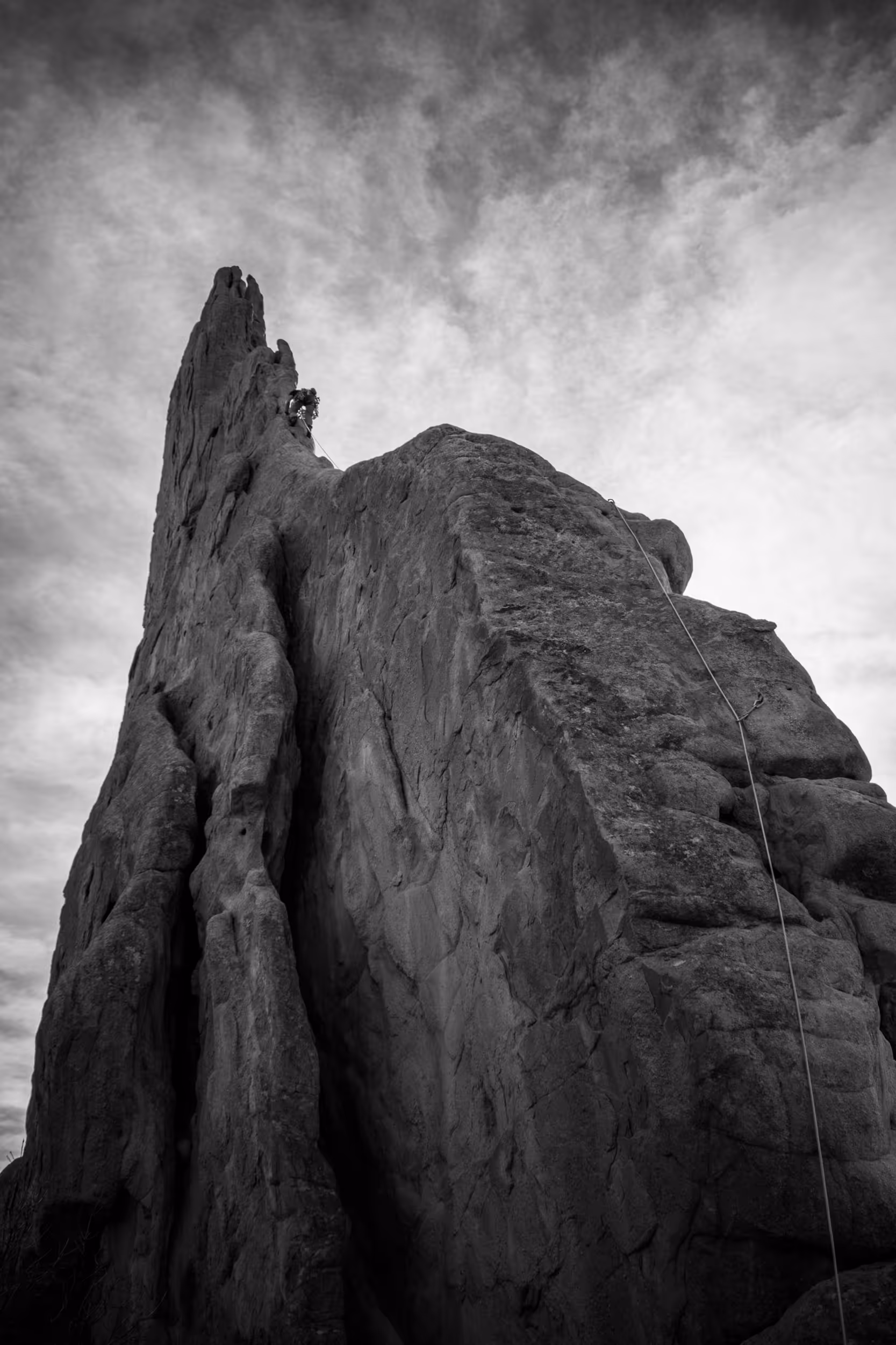 A black and white image of a climber navigating along a thin ridge 