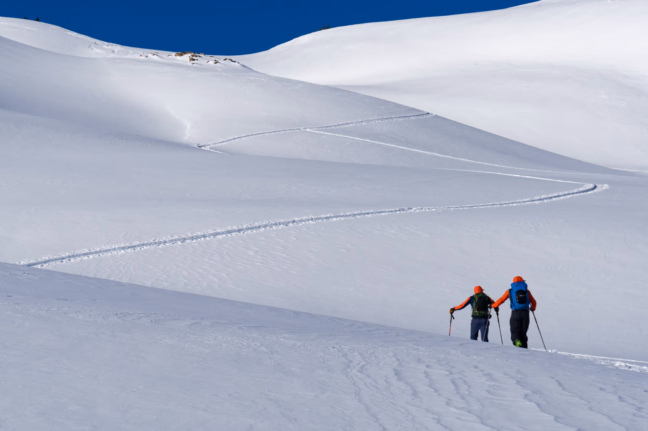 Some skiers skinning across a flat section of their ski tour with snow capped mountain in the background