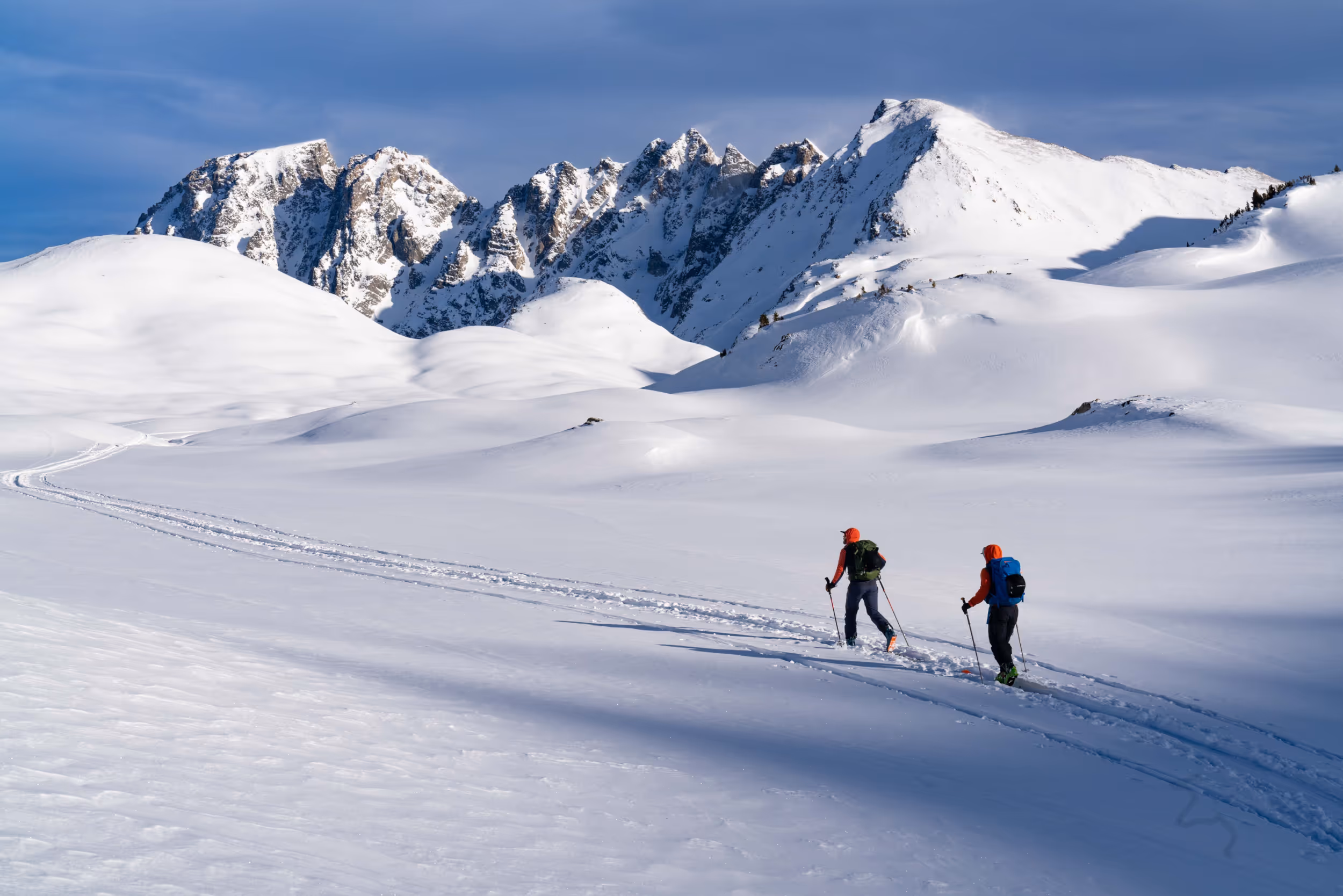Some skiers skinning across a flat section of their ski tour with snow capped mountain in the background