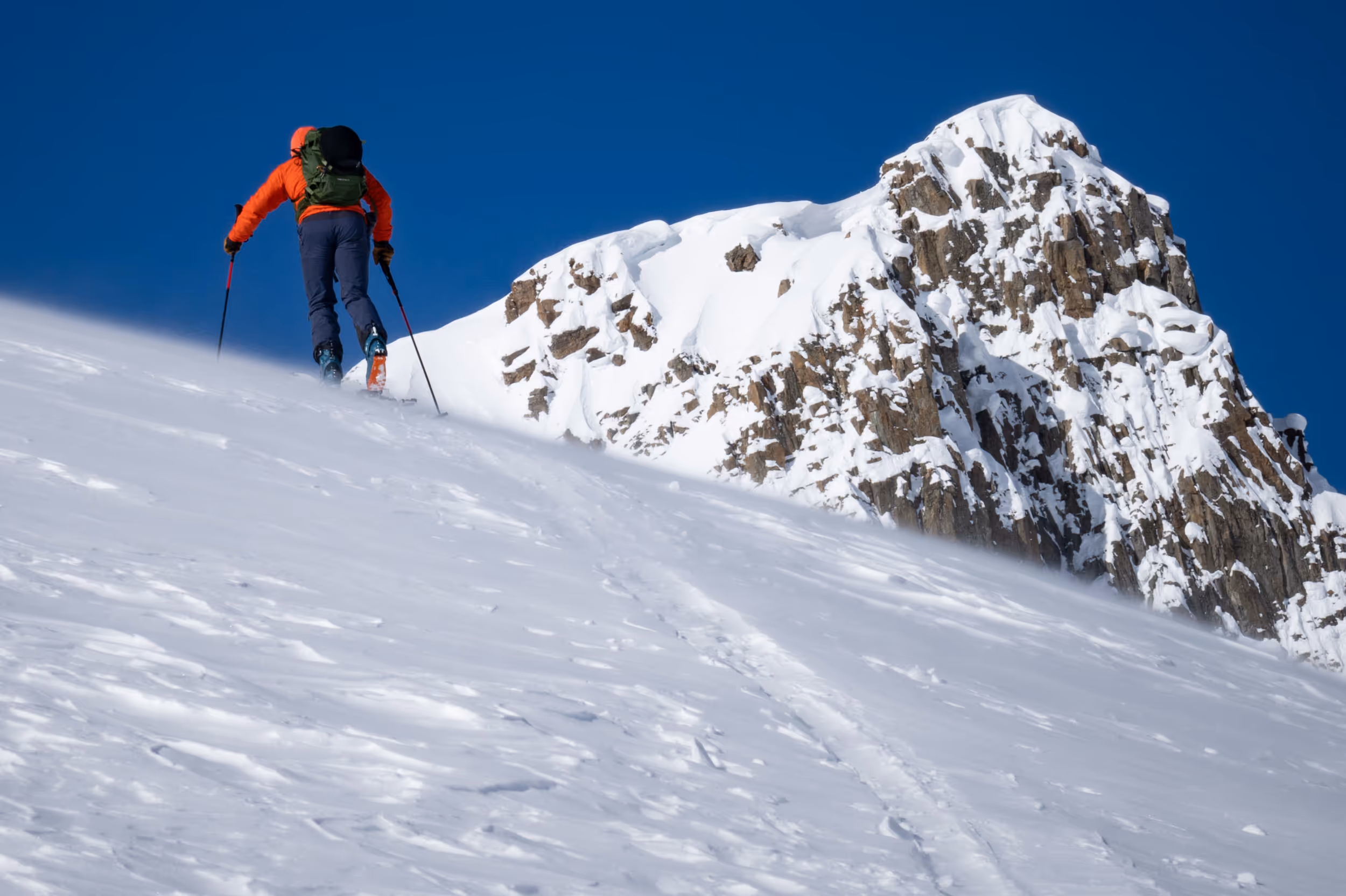 A skier getting to the top of a skin with a snow capped mountain in the background