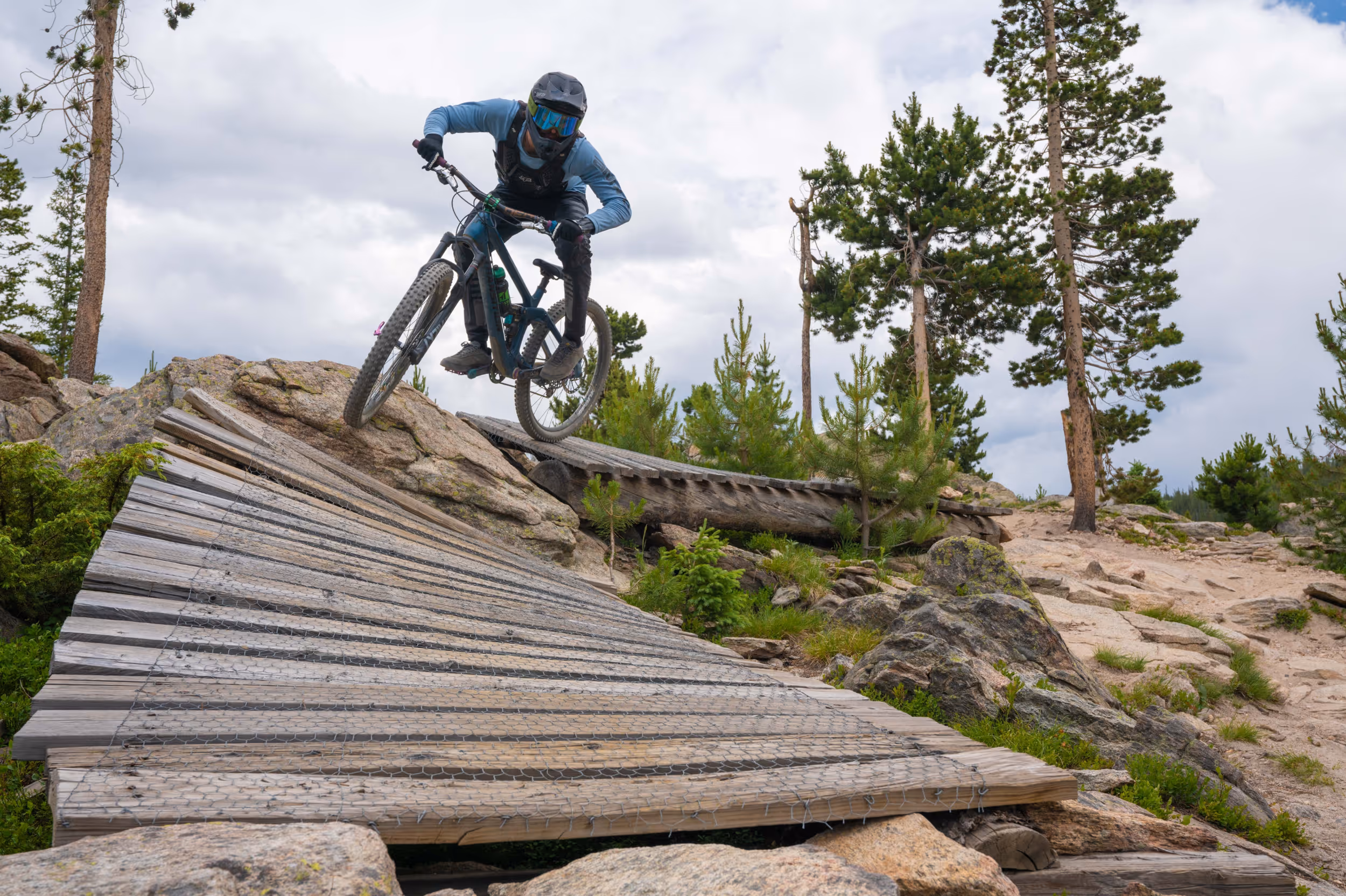 A mountain biker dropping in to a wooden berm section of trail 