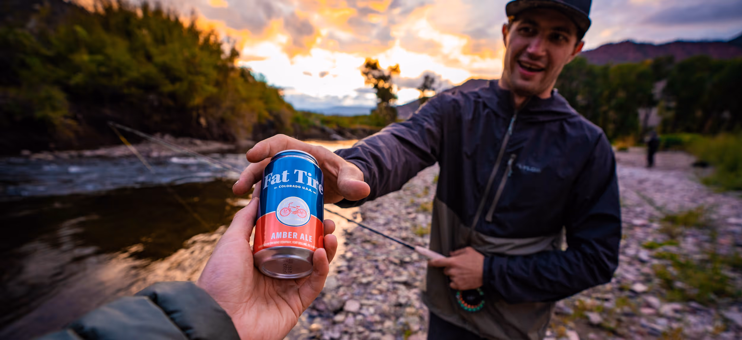 A man getting handed a Fat Tire beer with a sunset in the background