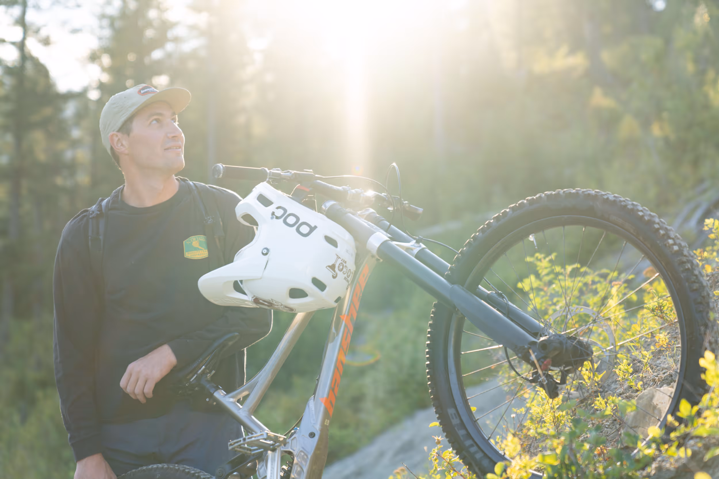 A man taking a break from mountain biking by leaning against his bike and enjoying the sun
