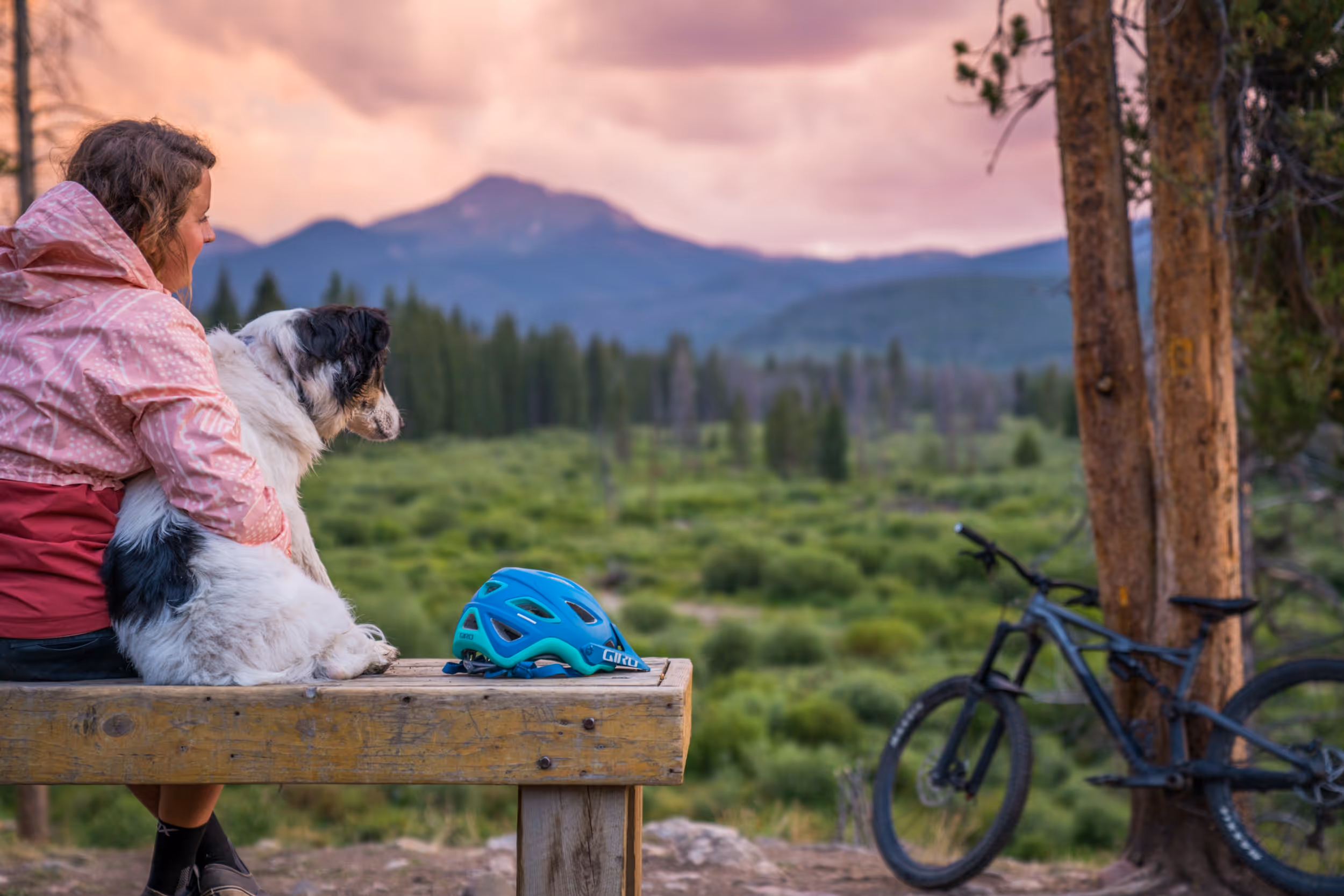 A woman and her pup enjoying the sunset from a bench overlooking the mountains