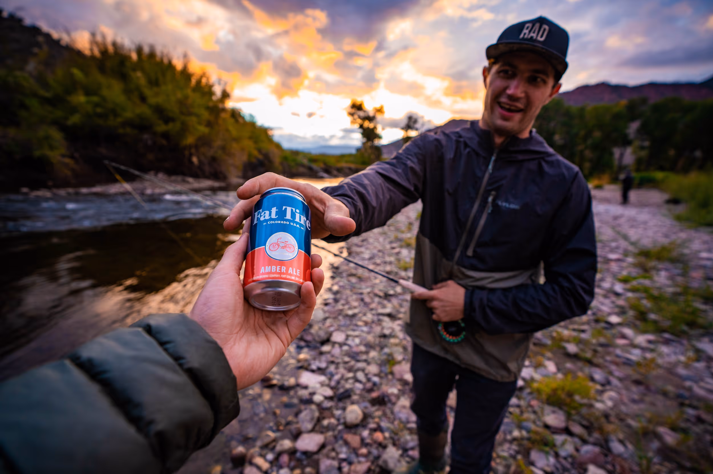 A fly fisherman passing his buddy Fat Tire beer 