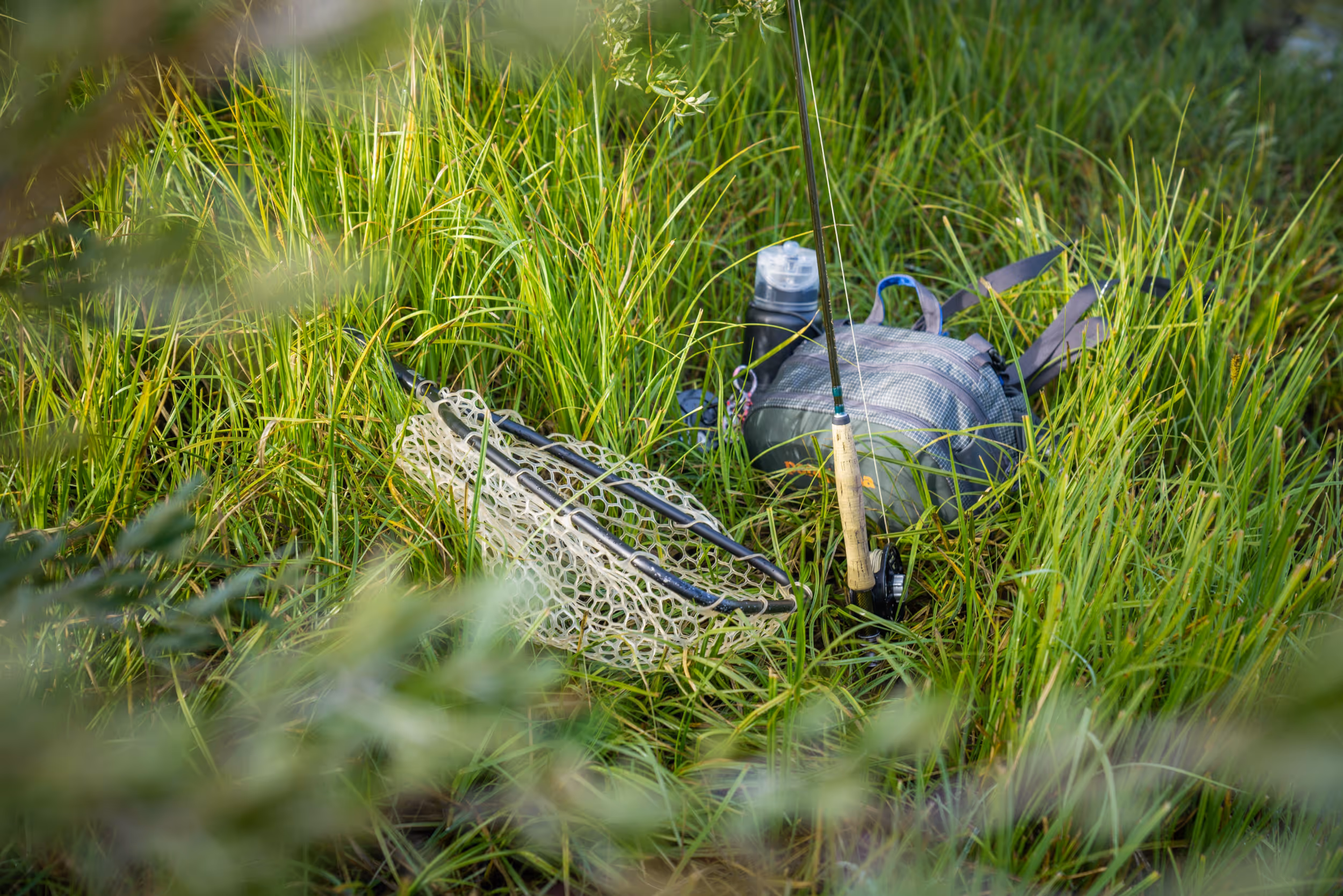 A fly fishing rod and net nestled in the damp grass 