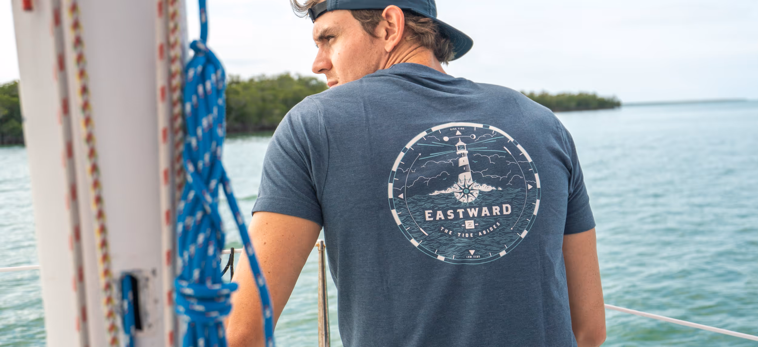 Man on a boat showing the back of his shirt. The back of the shirt has Eastward logo with a lighthouse