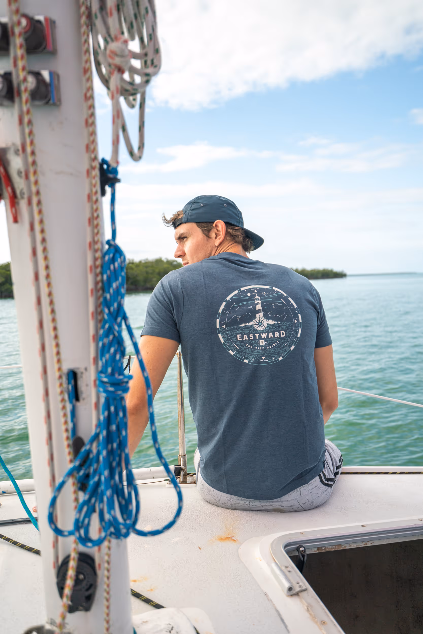 Man wearing Eastward t-shirt while sitting over the side of a sail boat. 