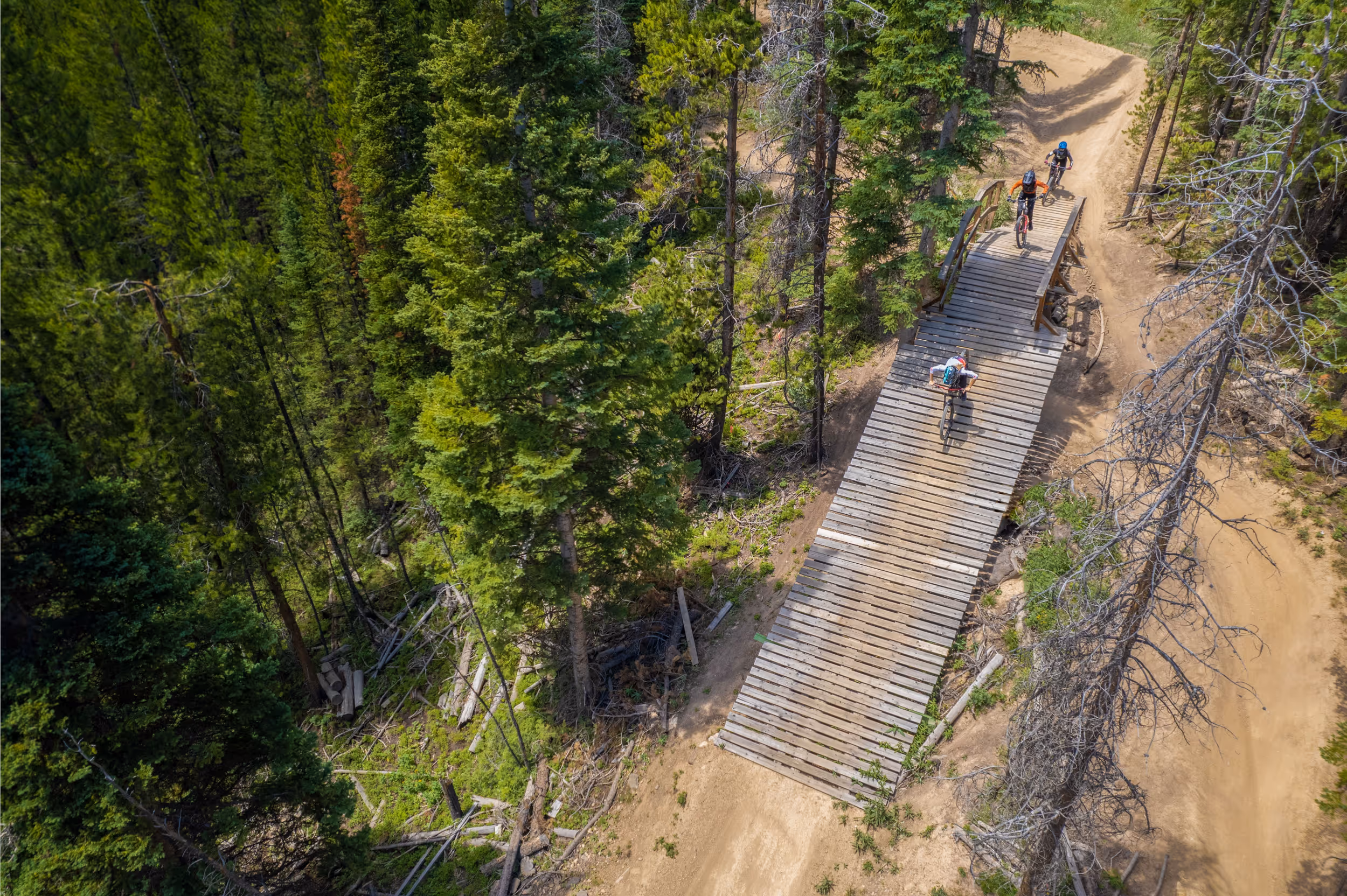 A crow eye view of 3 mountain bikers hitting a wooden jump 