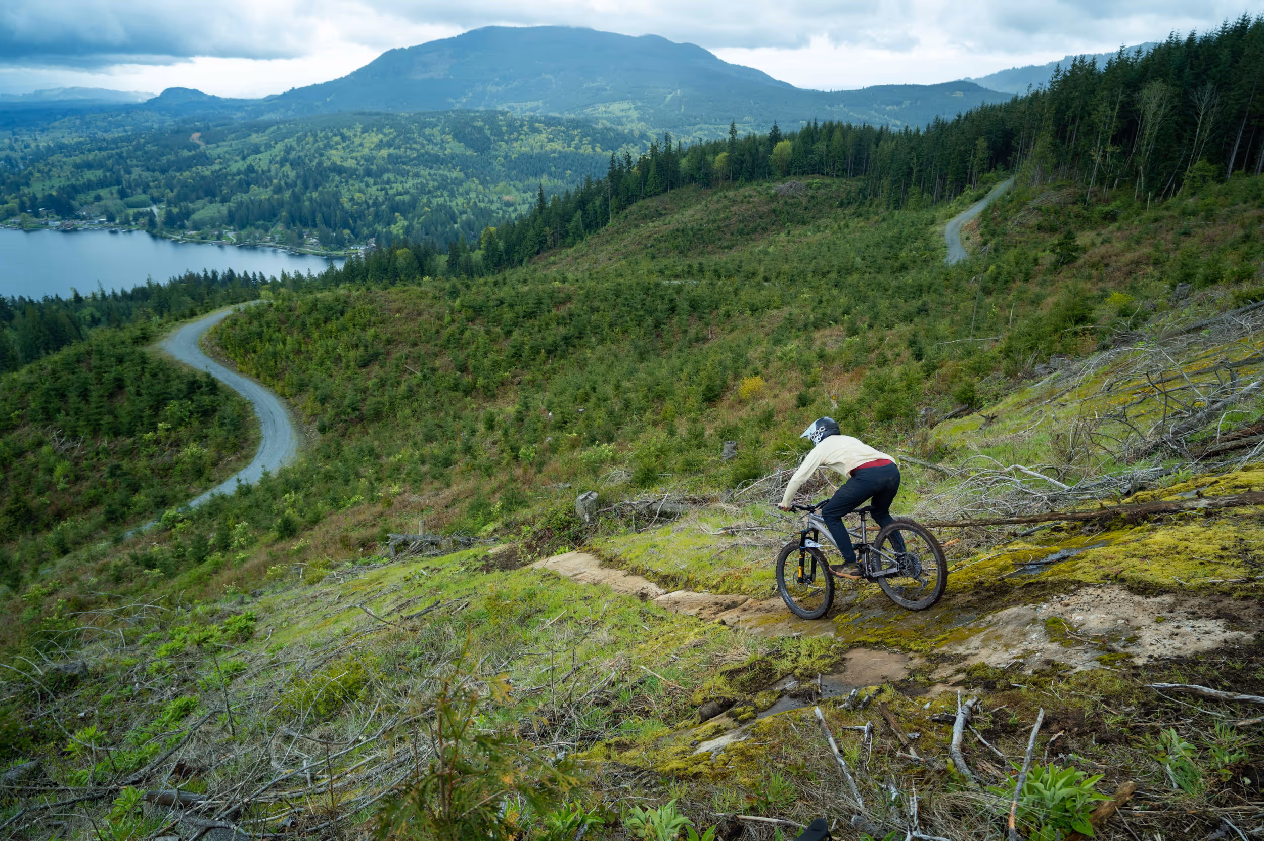 A mountain biker dropping into a steep section of trail with a lake in the background