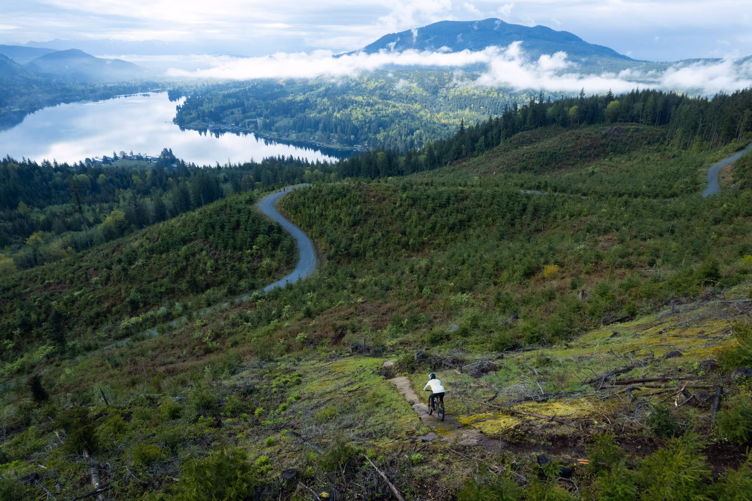 A mountain biker dropping into a steep section of trail with a lake in the background