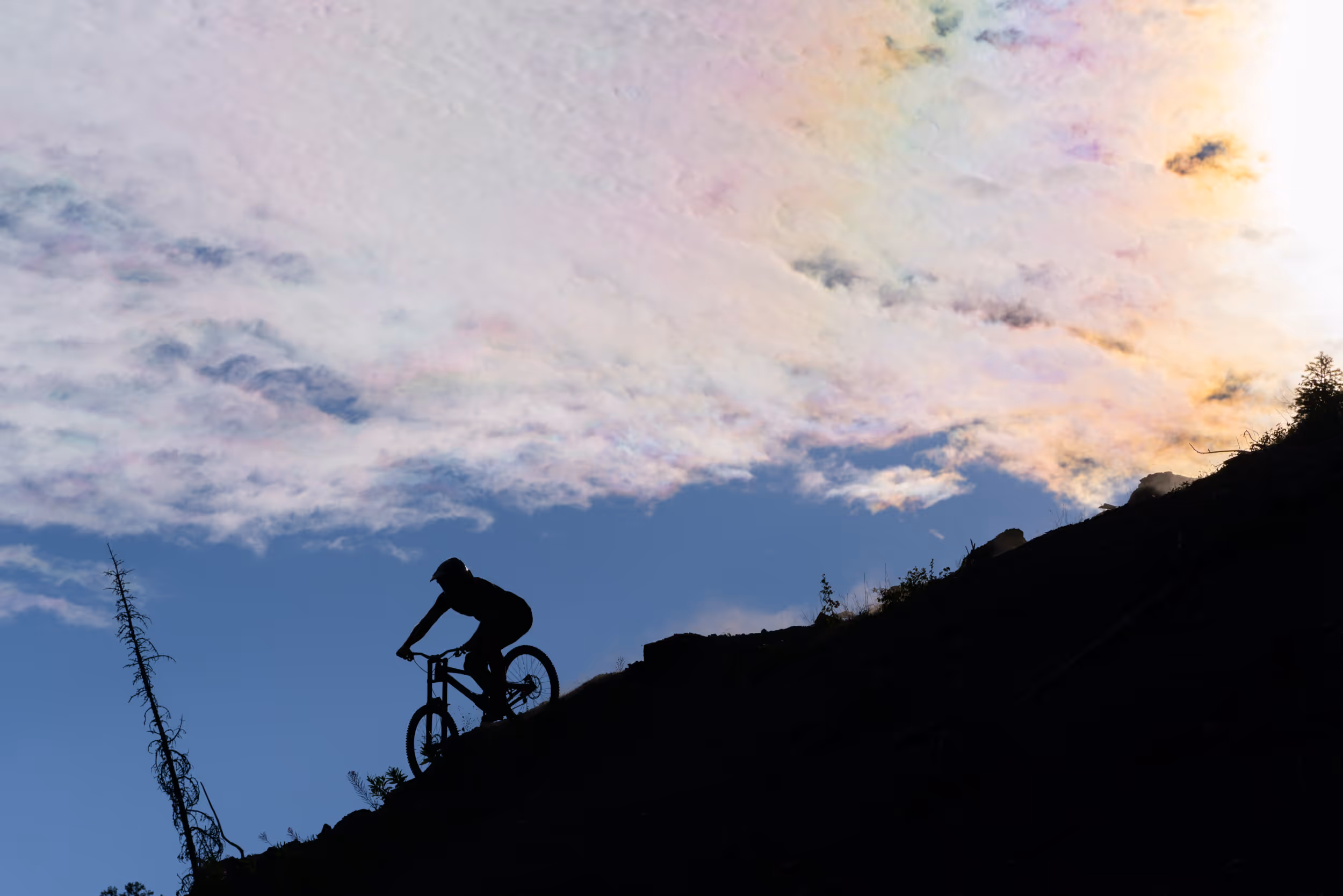 The outline of a mountain biker coming down a steep trail with a sunset in the background