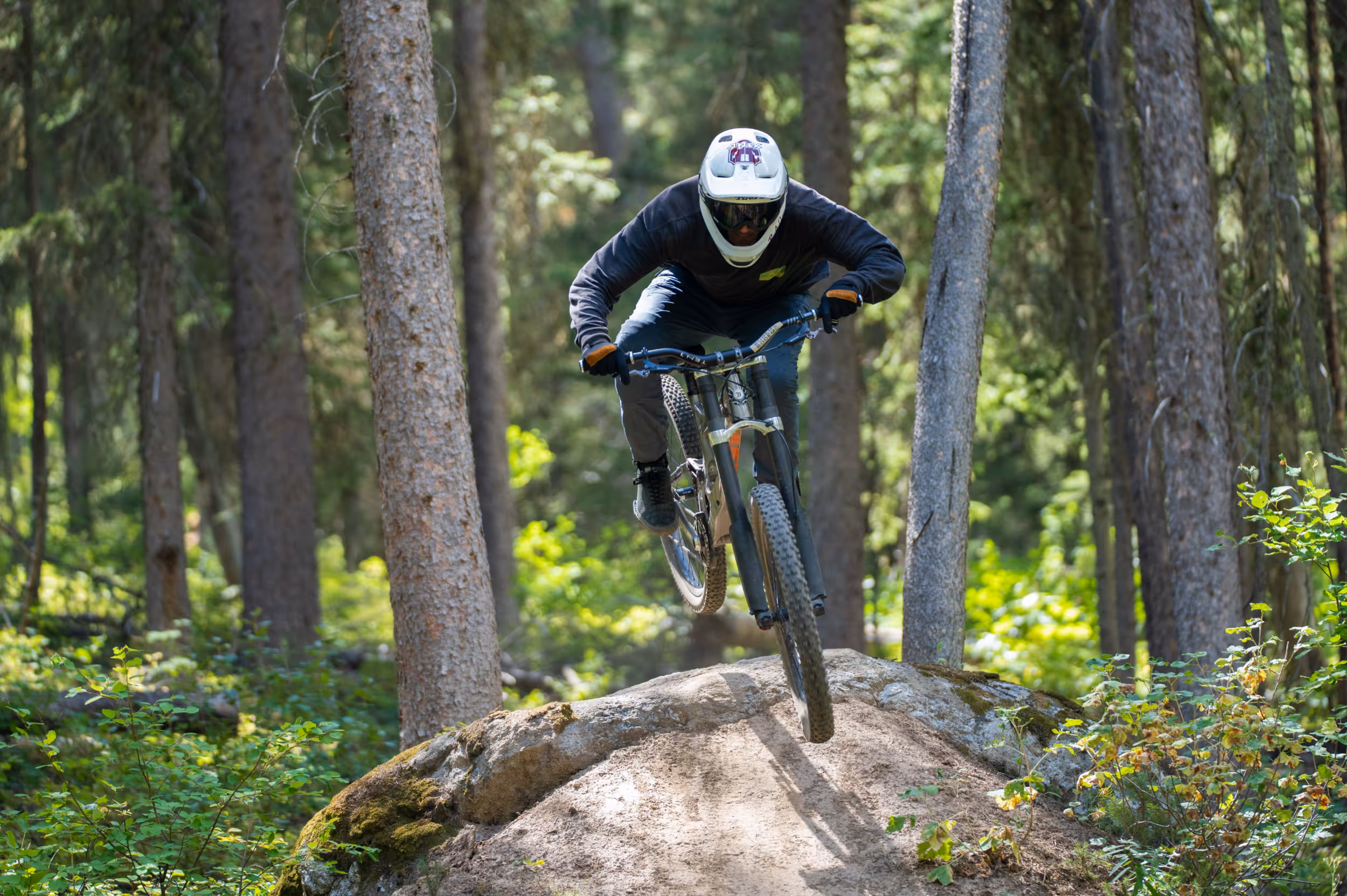 A mountain biker sticking the landing after jumping off a rock feature in the middle of  the trail