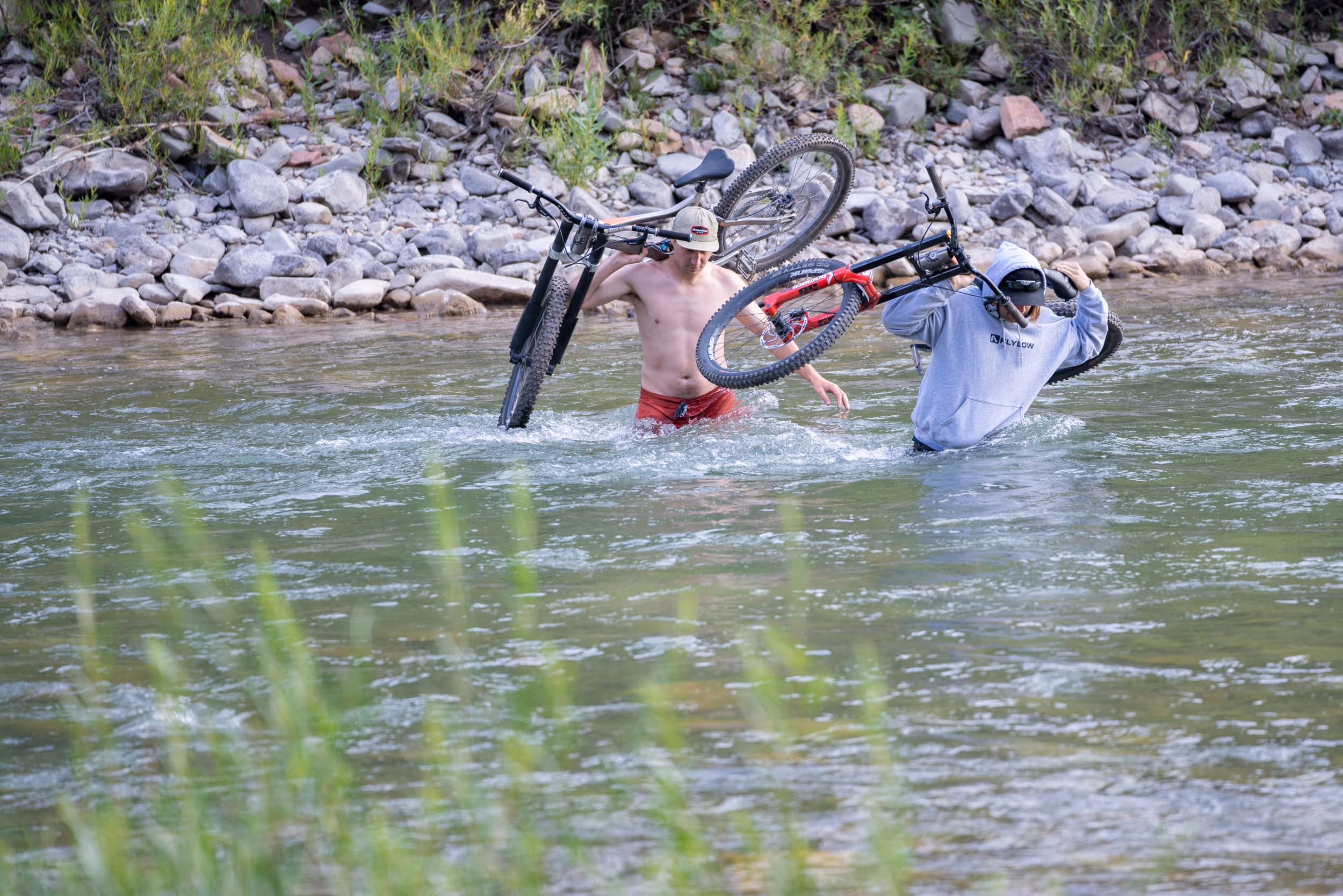 2 brave mountain bikers carrying their bikes across a river
