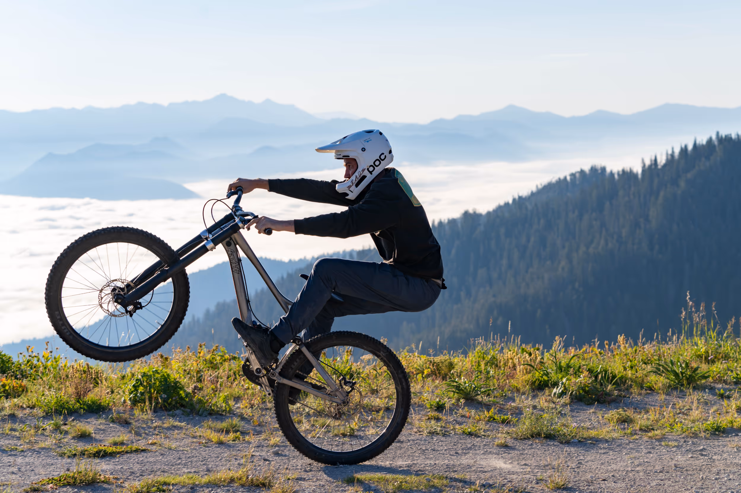 A mountain biker popping a sick wheelie in the foreground with a valley in the background 