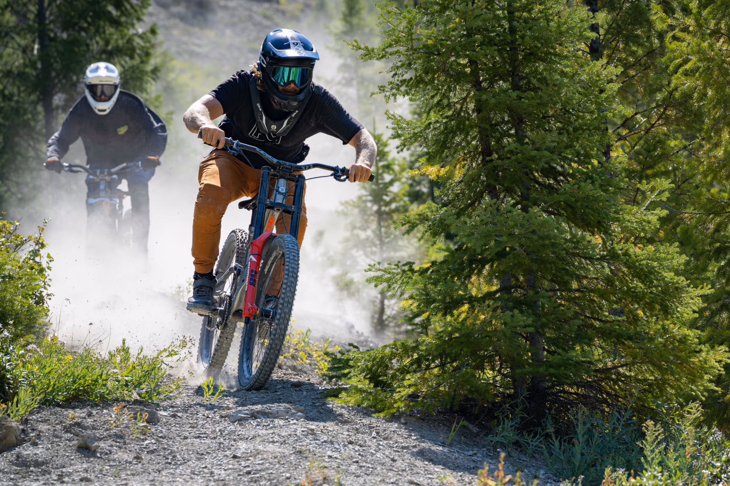 2 mountain bikers racing through a wooded section of a dusty trail